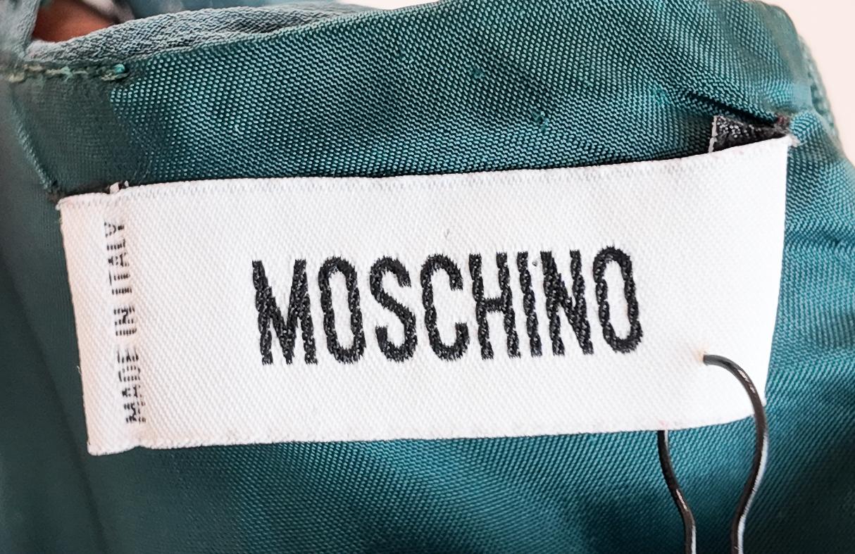 Confeccionado en lujosa seda en un intenso tono verde azulado, este vestido Moschino presenta elegantes detalles de lazo y un busto fruncido para una silueta refinada. Su perfecto color otoñal y su sofisticado diseño la hacen ideal tanto para