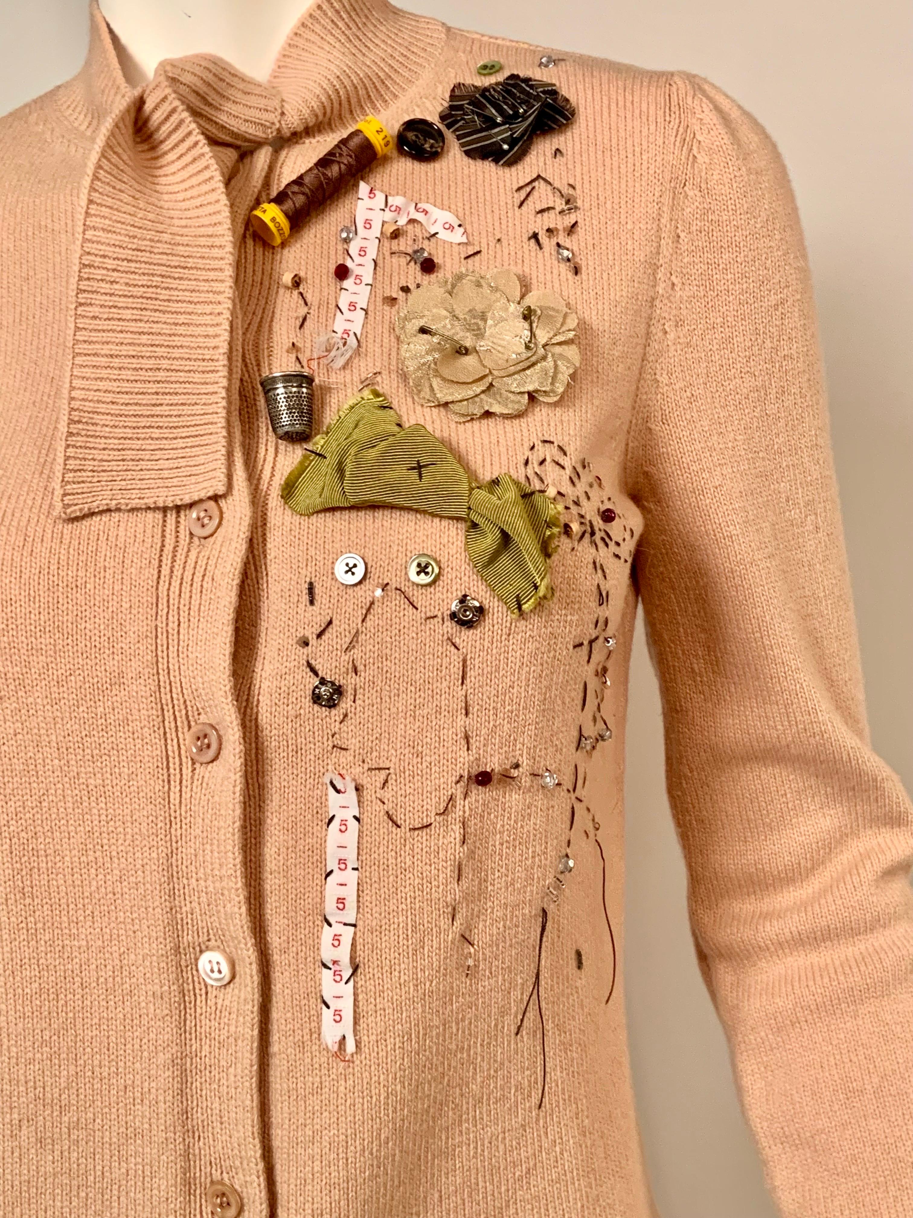 Moschino has taken this cashmere and wool blend cardigan sweater and had some fun with an appliqued sewing theme.  There are buttons, snaps, size tags, flowers, bows, a spool of brown thread, a thimble, beadwork and brown embroidery on the left