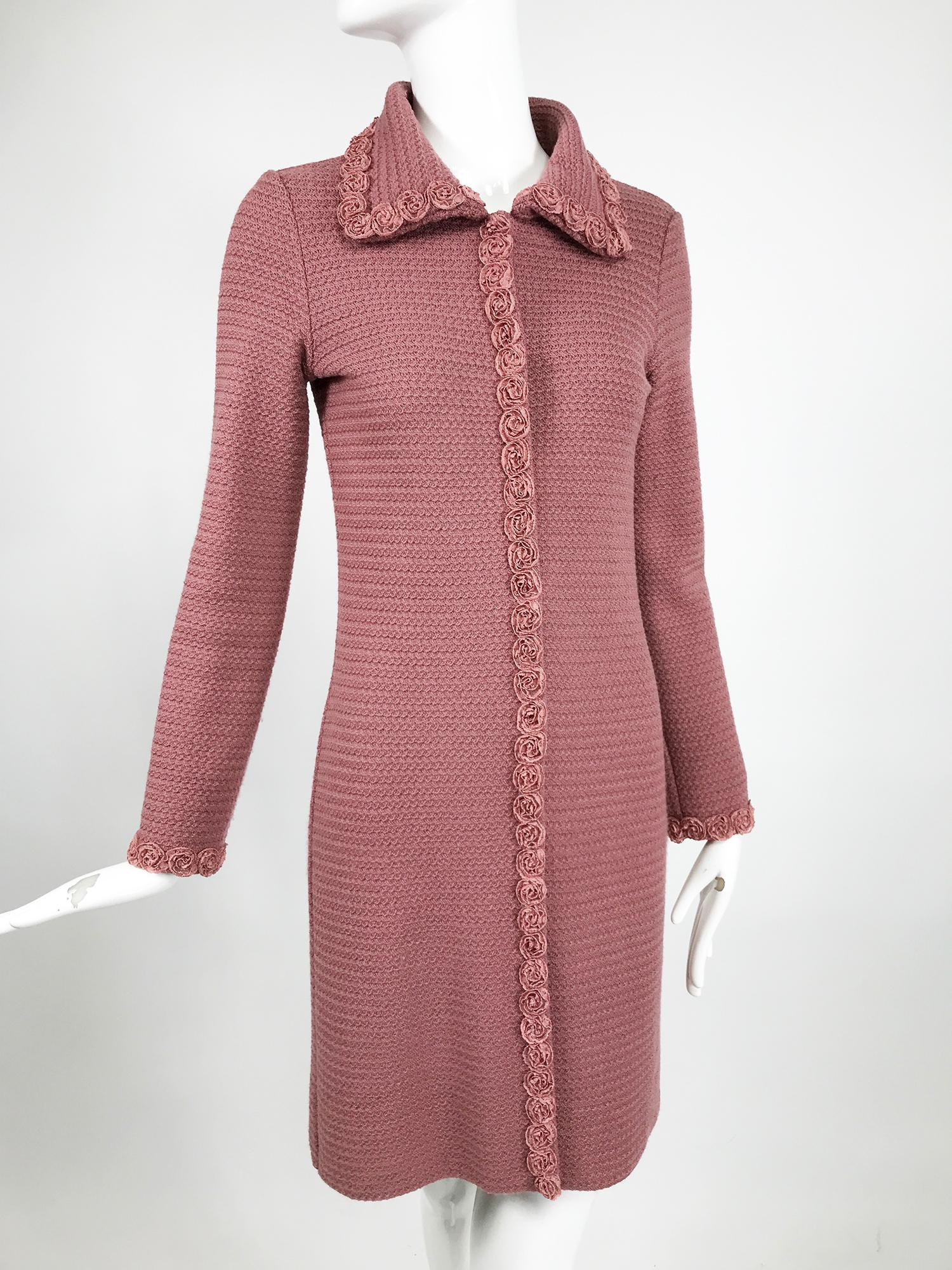 Moschino pink wool knit coat with rosette lace trims. Long sleeve coat closes at the front with hidden fabric covered snaps. The single breasted coat has a slim shape. Wing collar. The coat is lined in pink crepe, pink gros grain ribbon face the