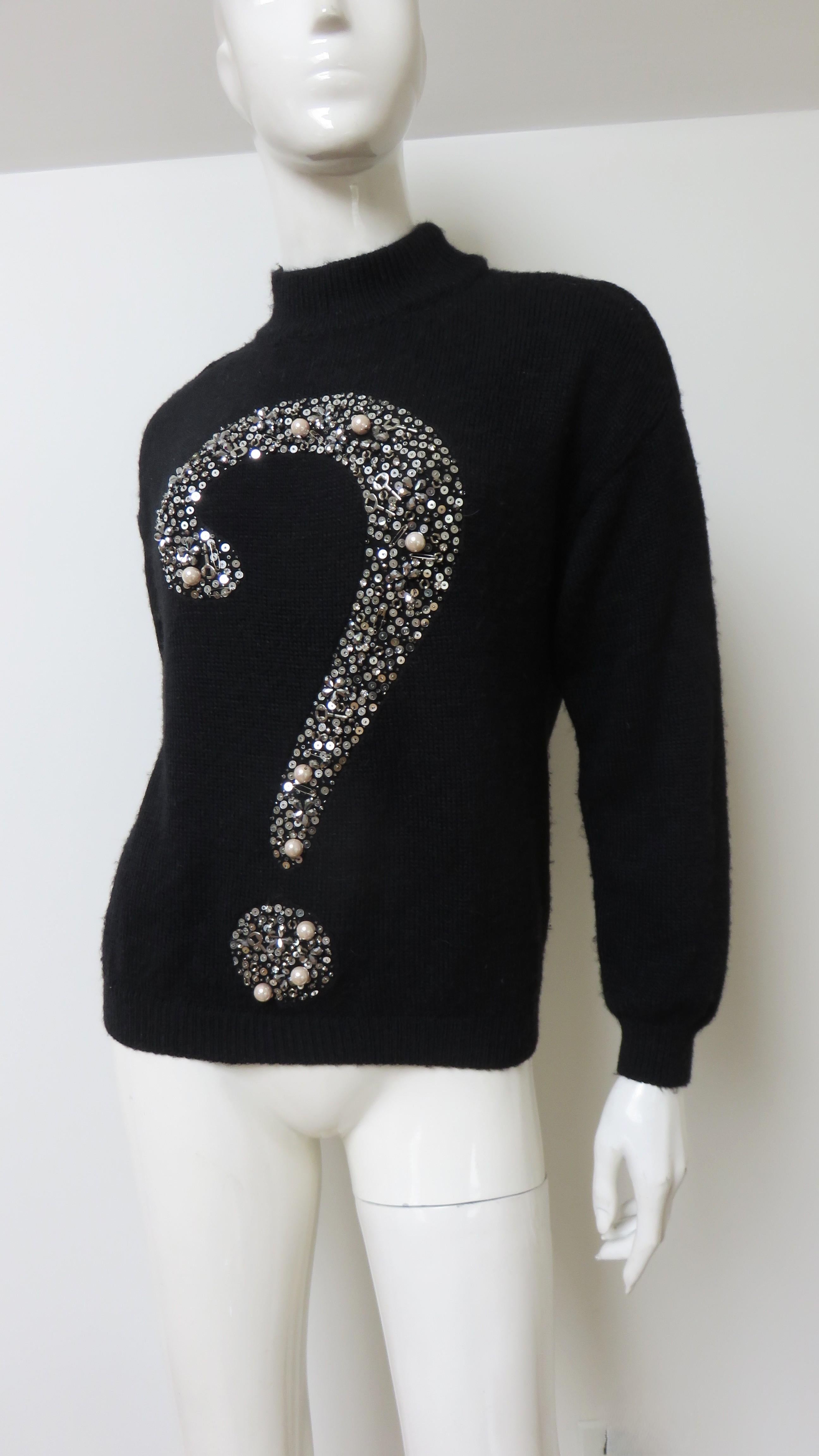 A gorgeous black wool sweater adorned with a large question mark in the front.  It has long cuffed sleeves, a crew neck and a large mixed metal question mark comprised of silver sequins, safety pins, keys and other small metal pieces.
Fits sizes