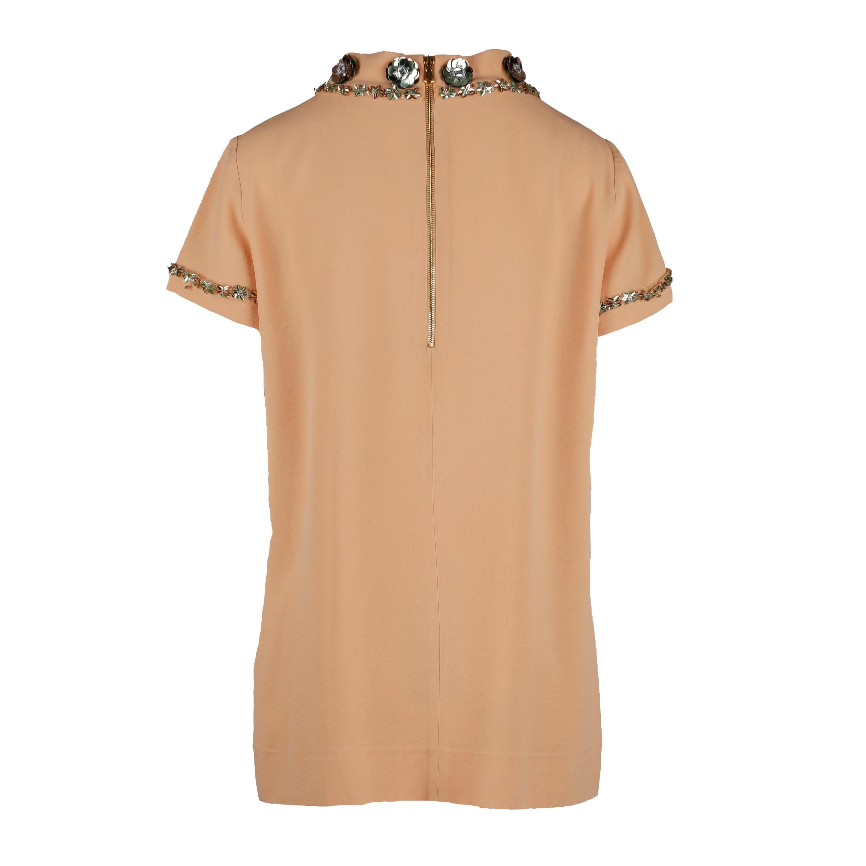 This Moschino blouse is the perfect summer staple. Crafted in a soft melon orange hue, this short sleeve blouse is adorned with a beautiful flower arrangement of sequins. The high crew neck and sleeve hem feature unique embellishment for a subtle