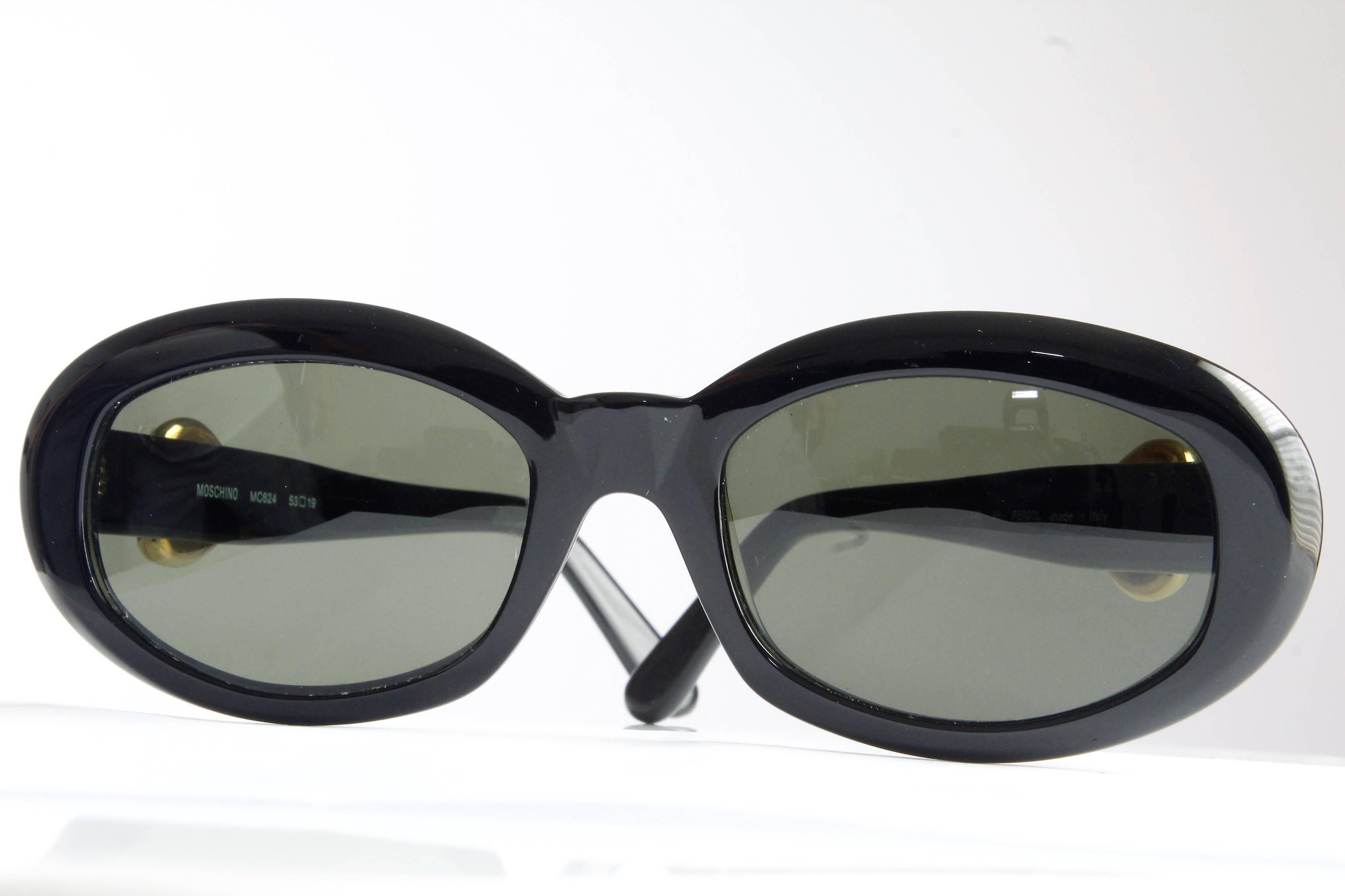 Une paire de lunettes de soleil pour femmes de Moschino et Persol Ratti, circa 1985.  Fabriqués en résine noire, ils comportent des cœurs en métal doré de chaque côté.  Usagé/vintage avec des signes minimes d'utilisation et d'usure.  Mesures :