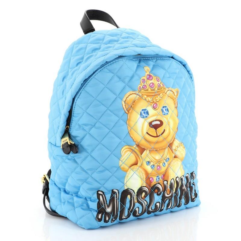 This Moschino Teddy Bear Backpack Quilted Printed Nylon Medium, crafted in blue quilted printed nylon, features adjustable backpack straps, teddy bear and signature print on front, and gold-tone hardware. Its zip closure opens to a black fabric