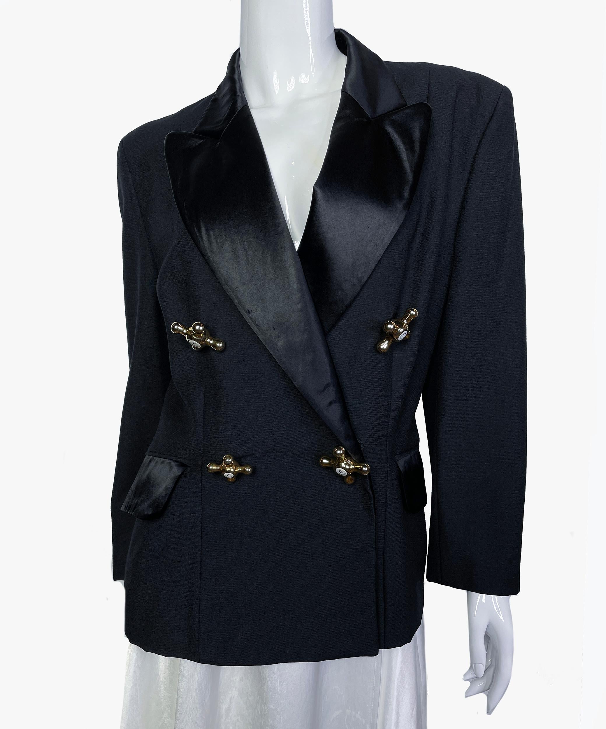 This iconic vintage Moschino jacket is crafted from a black virgin wool fabric with a silky/satiny collar and flap pockets.
The jacket features strong padded shoulders and a double-breasted closure with the iconic gold-tone faucet buttons.
Faucet