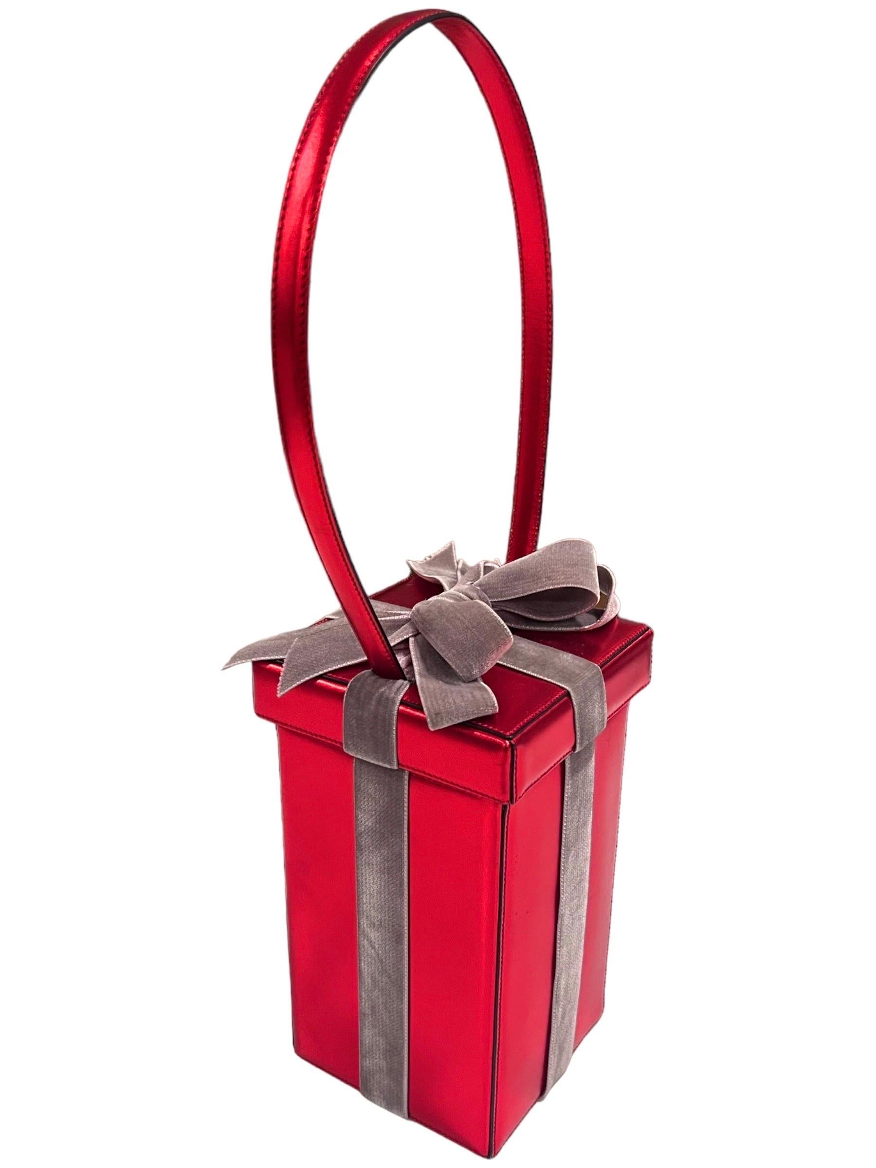 Moschino vintage whimsical red present gift box top handle bag.
Red metallic leather with a velvet bow.
To open the bag, the top lifts up but is attached to the bag by the leather straps.
Unique hanging tag stating “Happy 2000!” and “Present for the