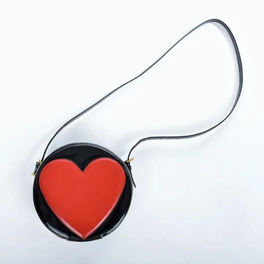 MOSCHINO VINTAGE REDWALL BLACK LEATHER RED HEART ROUND MESSENGER BAG

This black and red patent leather crossbody bag by Moschino showcases a red heart design at the forefront of its circular shape. It includes a top zip fastening, logo monogram