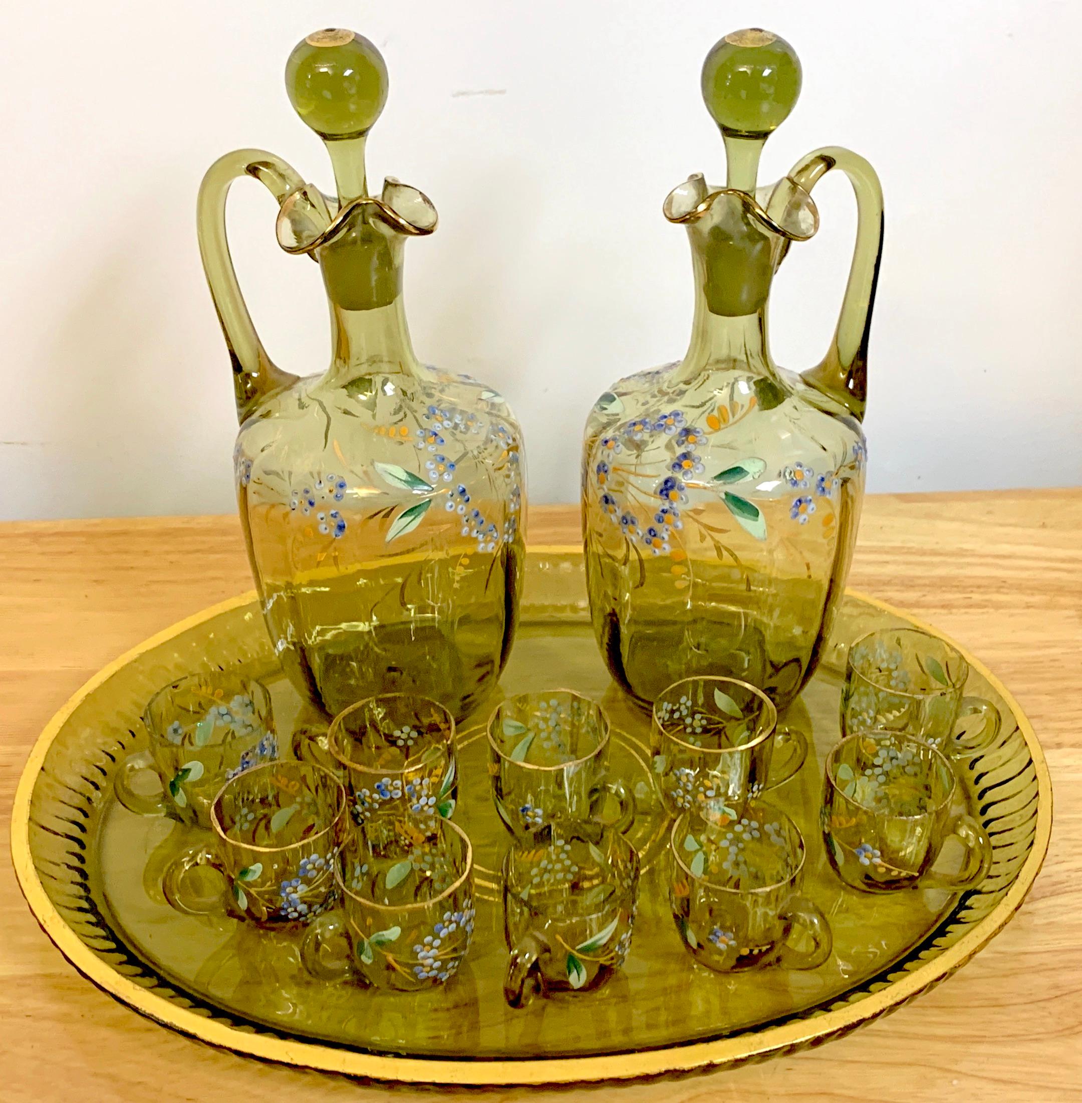 Moser Aesthetic enameled Cordial/ liquor set,15-pieces. Subtle olive green glass, with naturalistic enamel work with gilt highlights. Consisting of two handled decanters with stoppers, Ten handled cordials and one oval cut and gilt oval