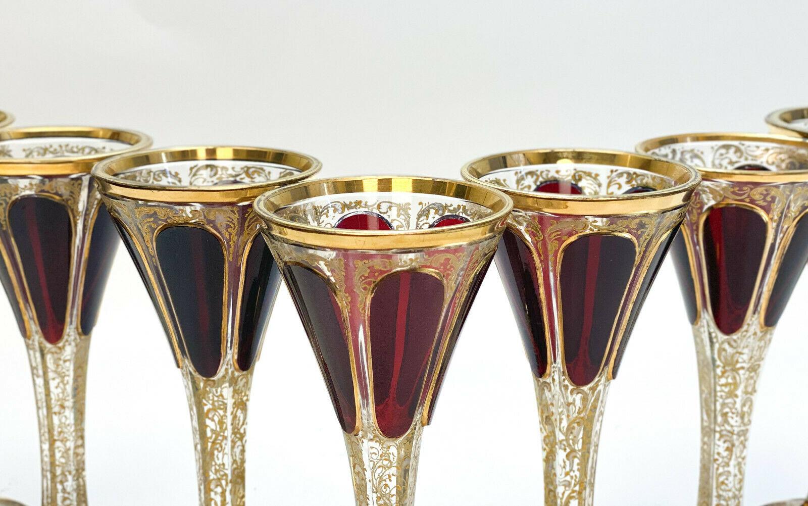 7 Moser cabochon & raised gilt garnet red to clear claret wine goblets, circa 1900. Gilt foliate scroll and beaded designs throughout with garnet red cabochon panels throughout the pieces. This is the antique version for which there are now numerous