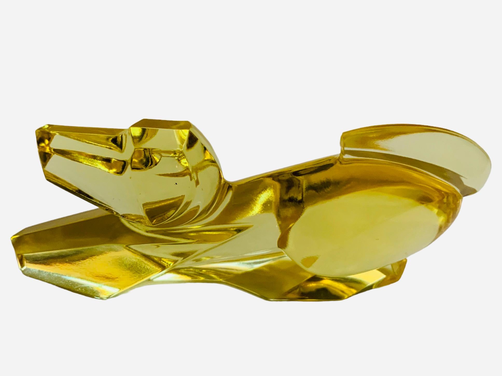 Se trata de una escultura de cristal Moser de color ámbar de un perro relajado con la cola hacia arriba. Debajo de la base está firmado Moser.