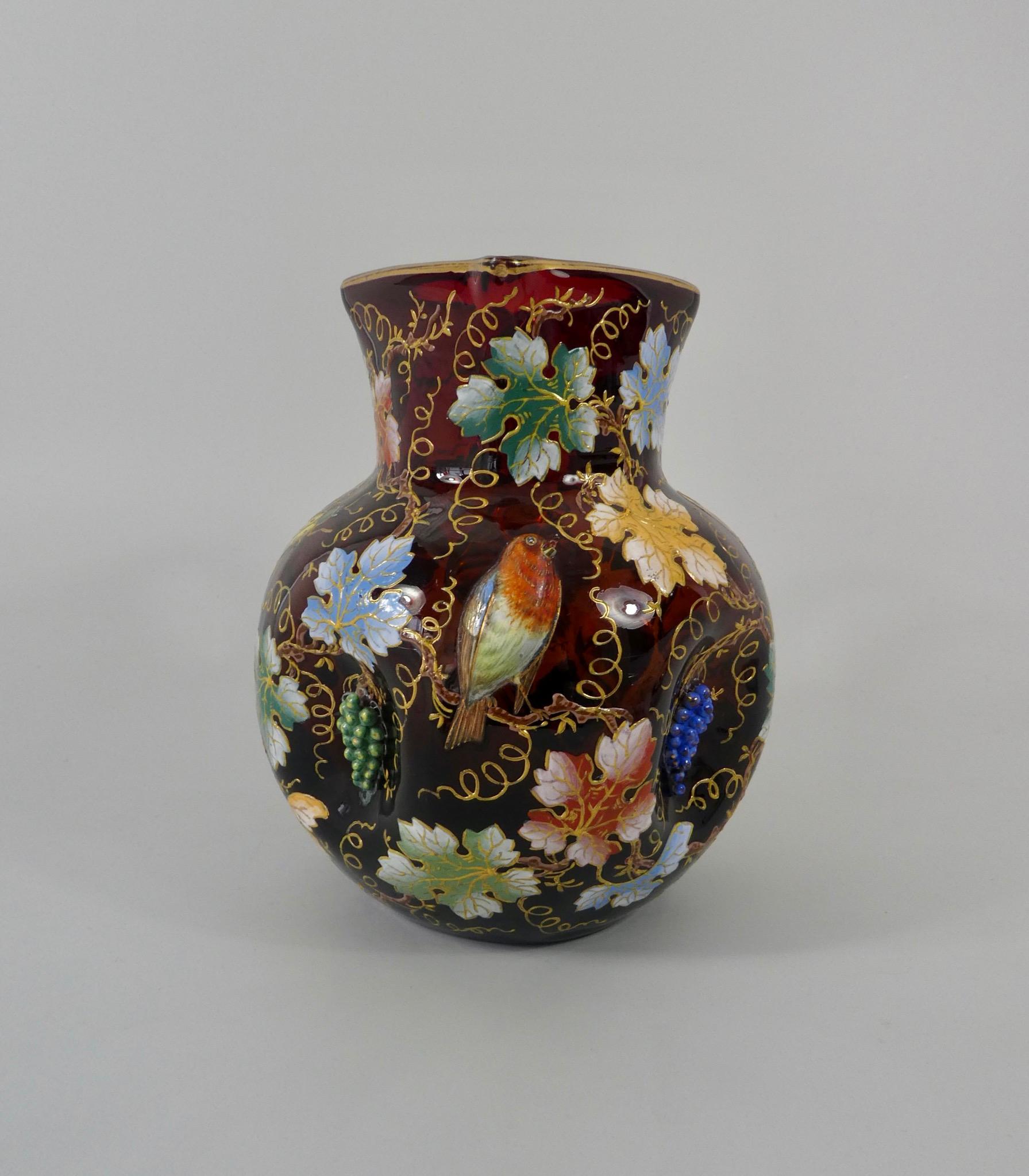Moser enamelled ruby glass jug, circa 1890. The squared globular jug, having four dimples moulded with grapes, suspended from a profusion of enamelled leaves and vines. A large robin is perched on a branch, beneath the spout, whilst two insects