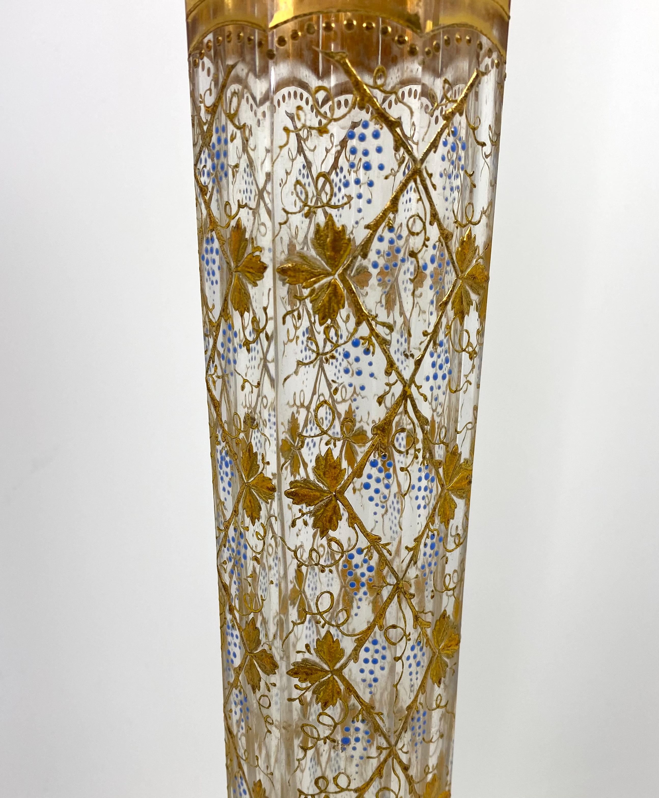 A Moser glass vase, gilt and enamel decoration, c. 1925. The tall octagonal shaped vase, gilded and enamelled with graping vines, suspended from trellis. The neck and foot decorated with a broad band of scrolling leaves, upon a gilt ground.
Printed