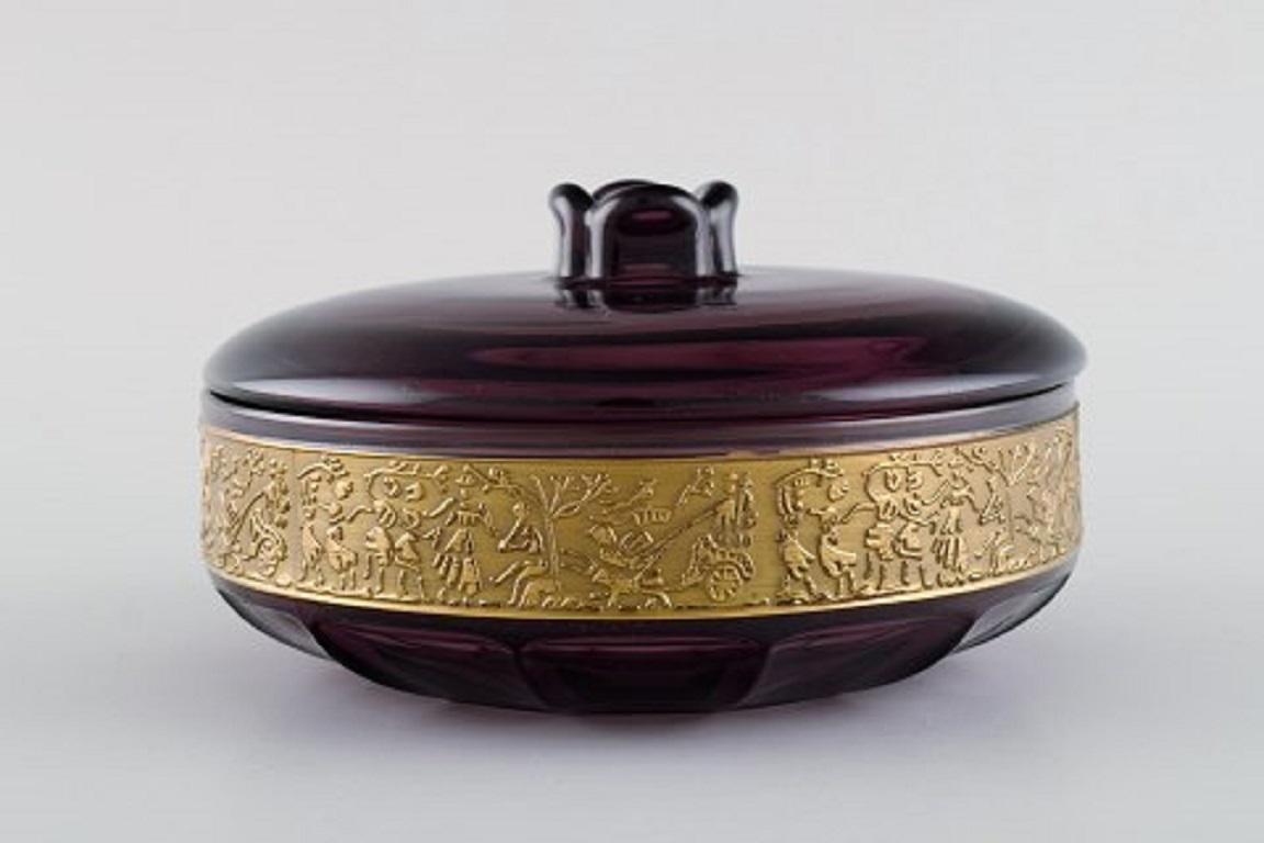 Moser Karlsbad Deckeldose aus violettem Kunstglas.
Messingfries mit der Szenerie,
1930er / 40er Jahre.
Maße: 15 x 8,5 cm.
In ausgezeichnetem Zustand.