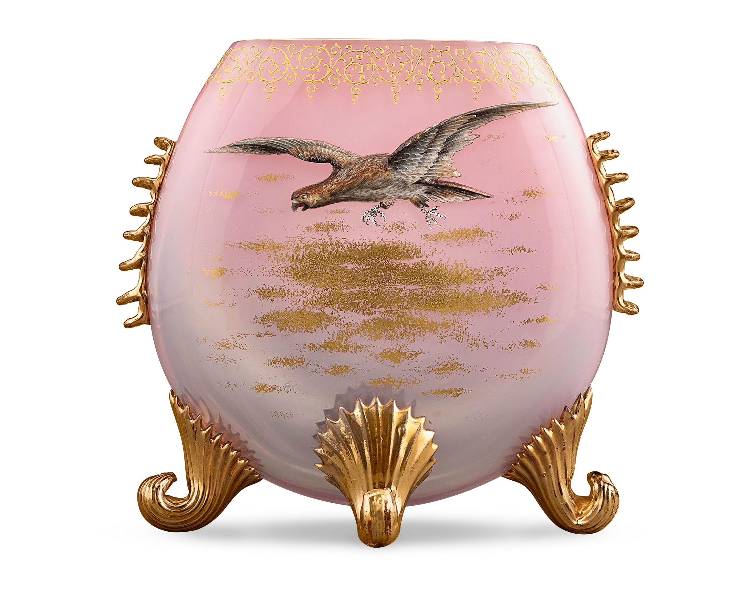 Il vetro opalescente rosa contraddistingue questo elegante vaso a cuscino Moser. Un falco scultoreo intricato scivola tra nuvole dorate, mentre rigaree dorate e piedi a spirale completano il design di questo meraviglioso vaso. Fondata nel 1857,