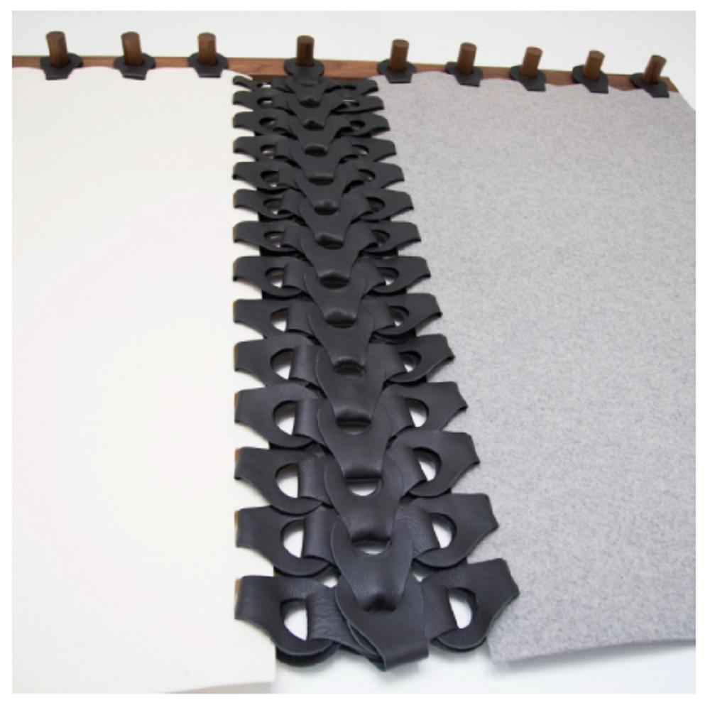 This Vertebrae Tapestry by Moses Nadel is hand-crafted from 100% Merino Wool Felt, Leather and Wood. 
This accent wall-hanging piece features a spine of die-cut leather woven between heavyweight wool felt panels with functional top links, designed