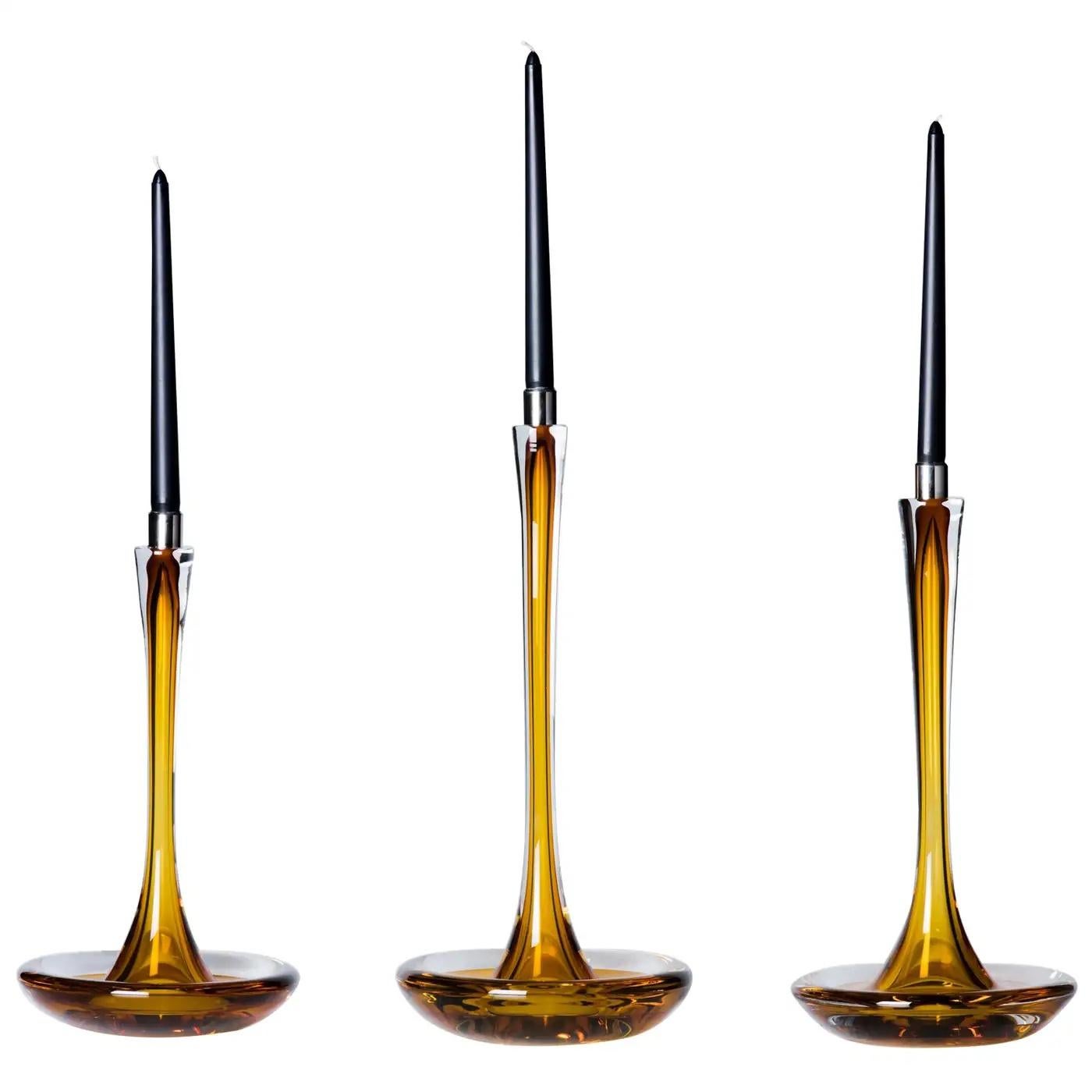 Contemporary American artist Moshe Bursuker's hand-sculpted solid set of three amber glass candleholders with a mirror finished stainless steel cup. These pieces are uniquely handcrafted to show off the nature of the material they are made from.