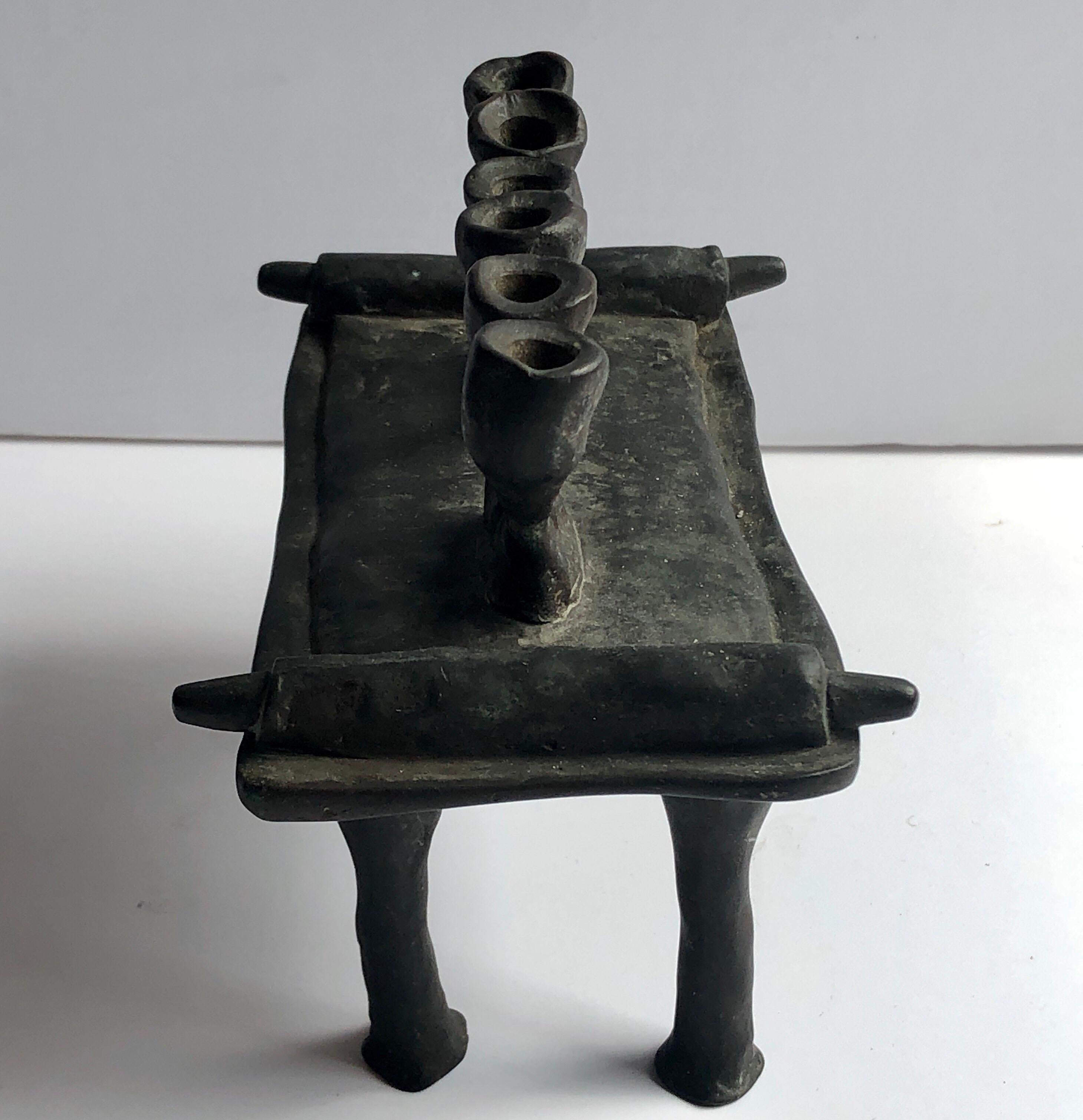 In the shape of two hebrew letters Shin. in the form of a torah scrollon a table. This surrealist sculpture is a tribue to the six million Jews who perished in the Holocaust. 

Moshe Oved (aka Edward Good) was a Polish-British, jeweler, artist,