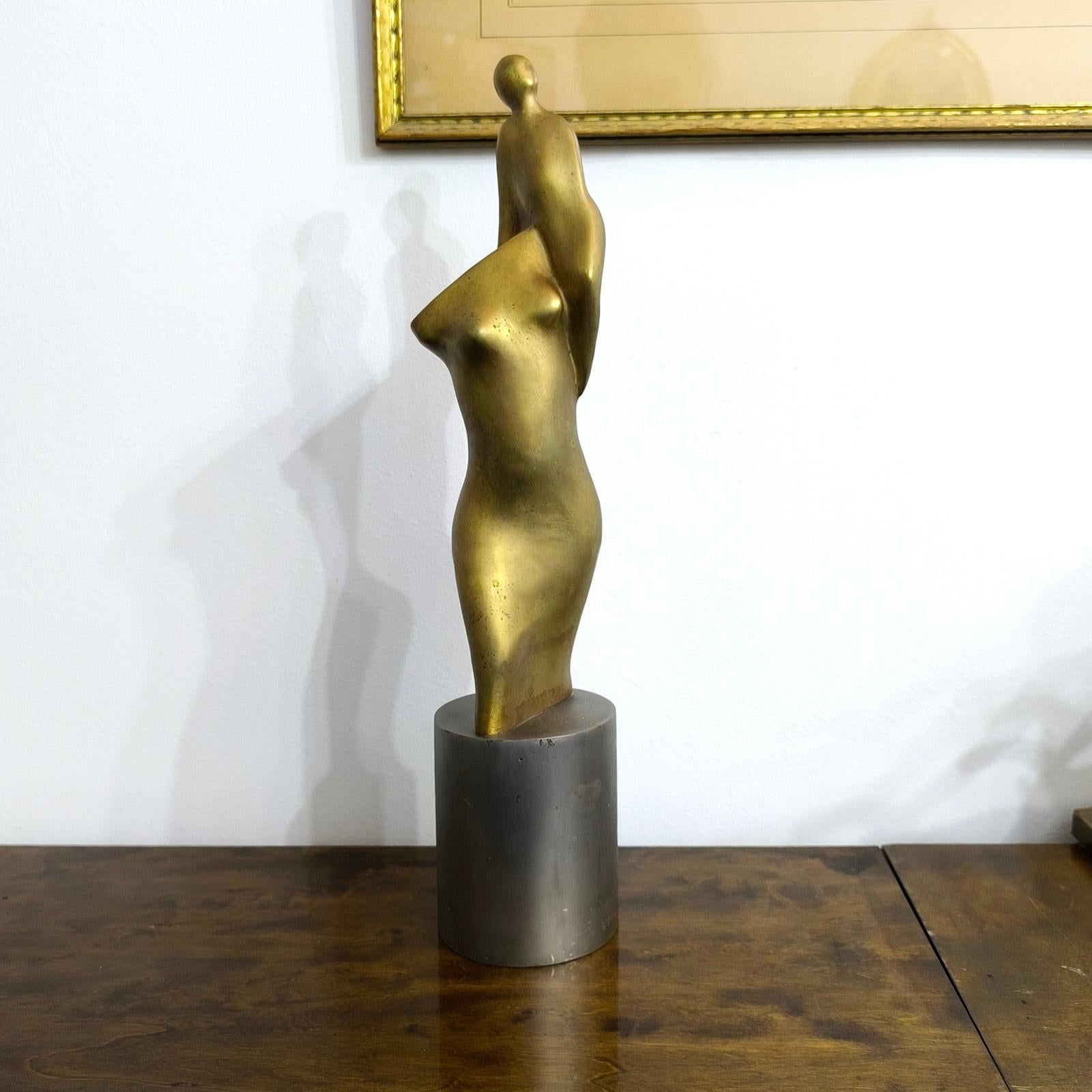 Questa composizione figurativa modernista è un pezzo accattivante che raffigura una donna che porta un bambino sulla spalla. Realizzata in bronzo, la scultura presenta una patina bicolore che aggiunge profondità e contrasto all'opera. Sul retro si