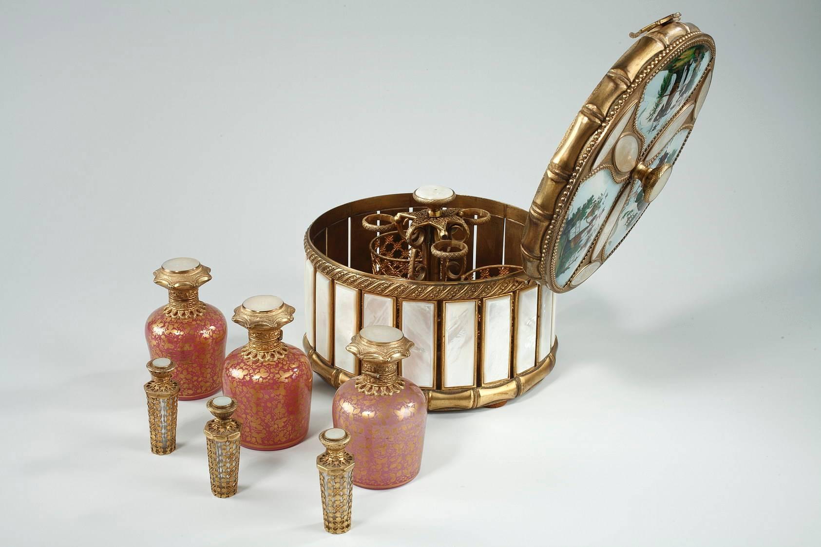 Round perfume box containing six flasks. The three larger flasks are in pink opaline accented with gold foliage, and the other three smaller flasks are in crystal and gilt bronze that is decorated with openwork floral motifs. The body of the box is