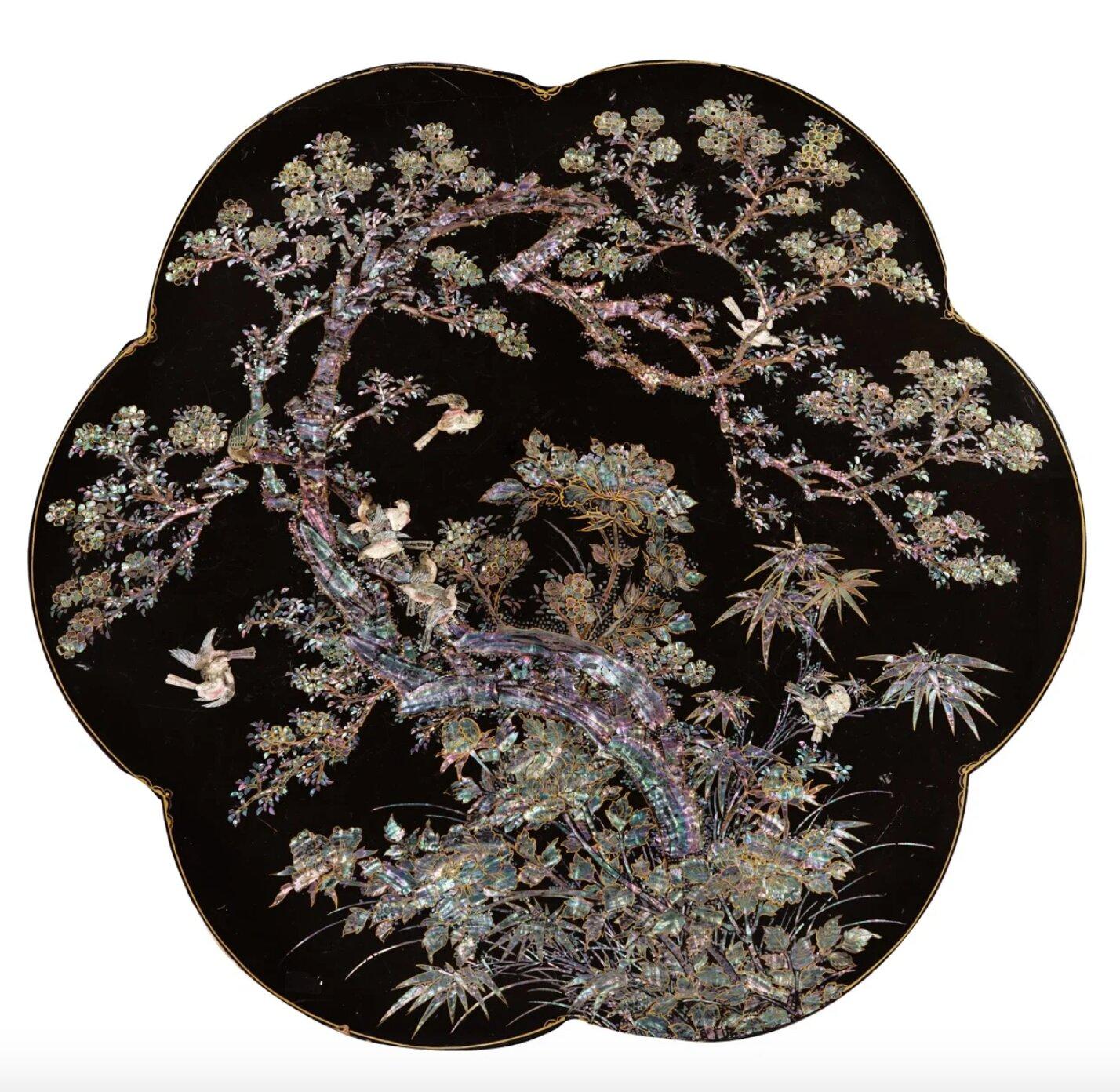 A Japanese export lacquer tripod table with feet shaped as bats
Nagasaki, 1850-1860

H. 73 x diam. 108 cm

The six-lobbed top is decorated with reverse-painted mother-of-pearl in a sprawling motif of plum blossom, bamboo, and peonies,