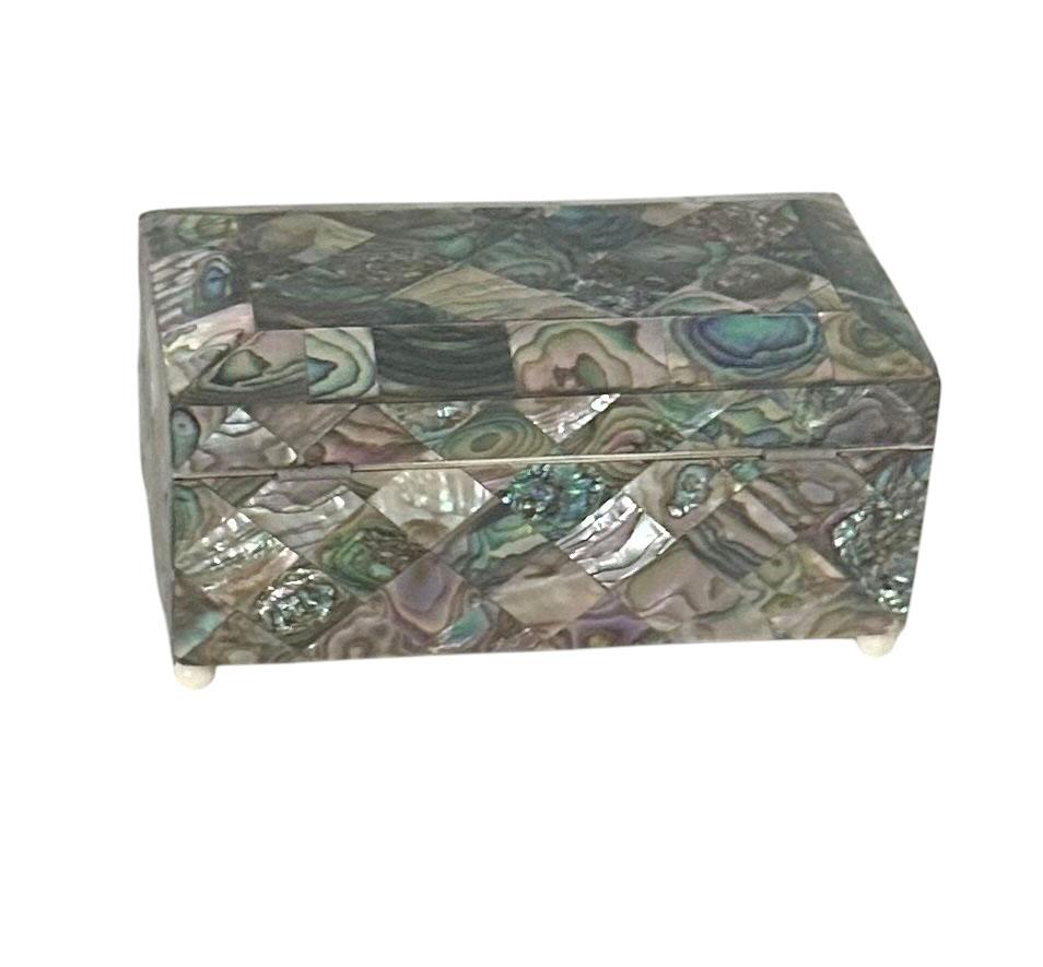 Exquisita caja de finales del siglo XIX con finos detalles de nácar, pies de imitación de marfil y un borde a juego que enmarca la pieza con elegancia clásica. El interior está lujosamente forrado en terciopelo profundo y ofrece una profundidad de