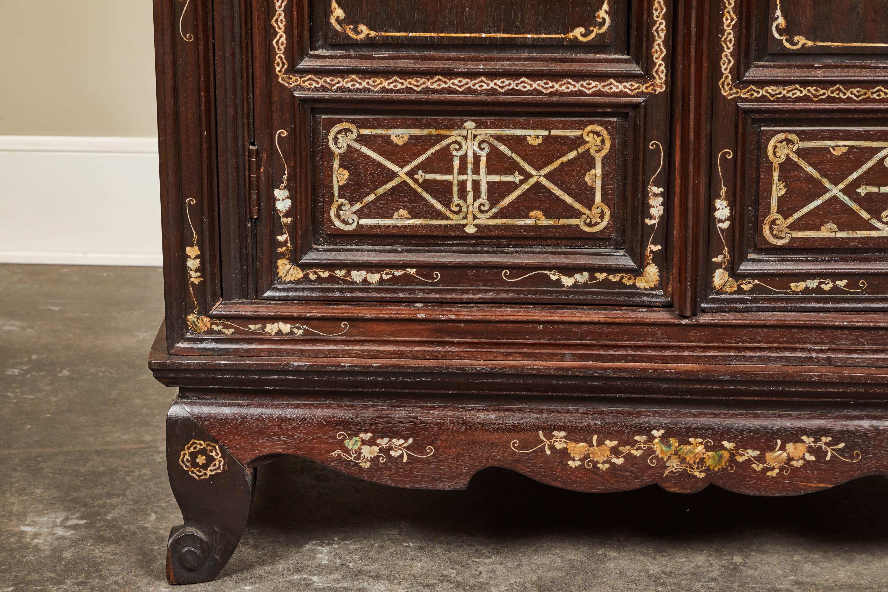 A solid rosewood cabinet with the front richly inlaid with mother of pearl depicting birds and a delicate floral motif. Made in Vietnam for the export market. The two doors open to reveal a compartment divided by two shelves. All on four slightly