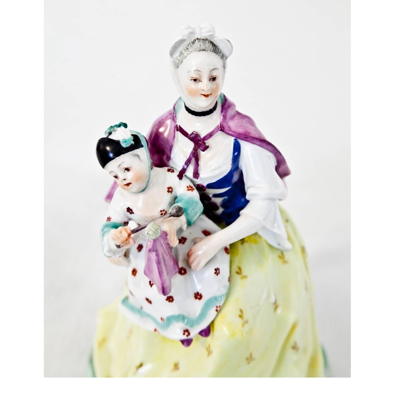 Porcelain figurine of a mother with child on her lap, sitting on a landscape base. Marked on the bottom with a blue tie shield of the Vienna porcelain manufactory.