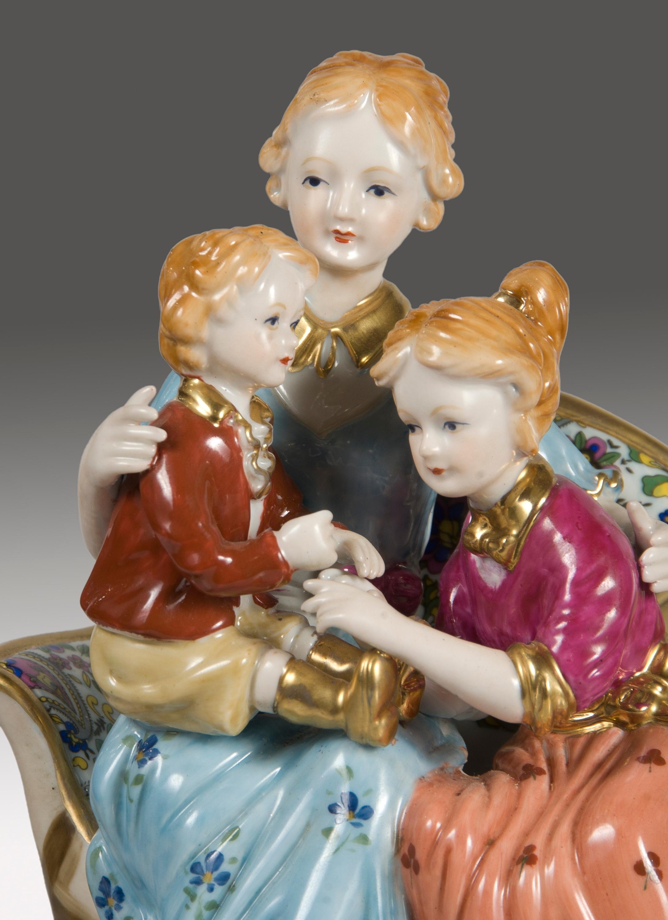 Enameled porcelain figure inspired by 18th century works of outstanding manufactures such as Sèvres, showing a lady sitting in an sofa and accompanied by a girl and a younger child. On the base there are details enhanced in gold similar to those
