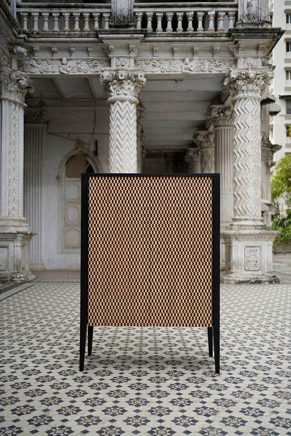 Der Motley Bar Cabinet von Ariane Thakore Ginwala ist ein exklusives Stück mit aufwändigen Holzarbeiten und Designdetails. Dieser Schrank ist ein modernes Kunstwerk aus der Mitte des Jahrhunderts mit einem von Hand eingelegten Schachbrettmuster aus