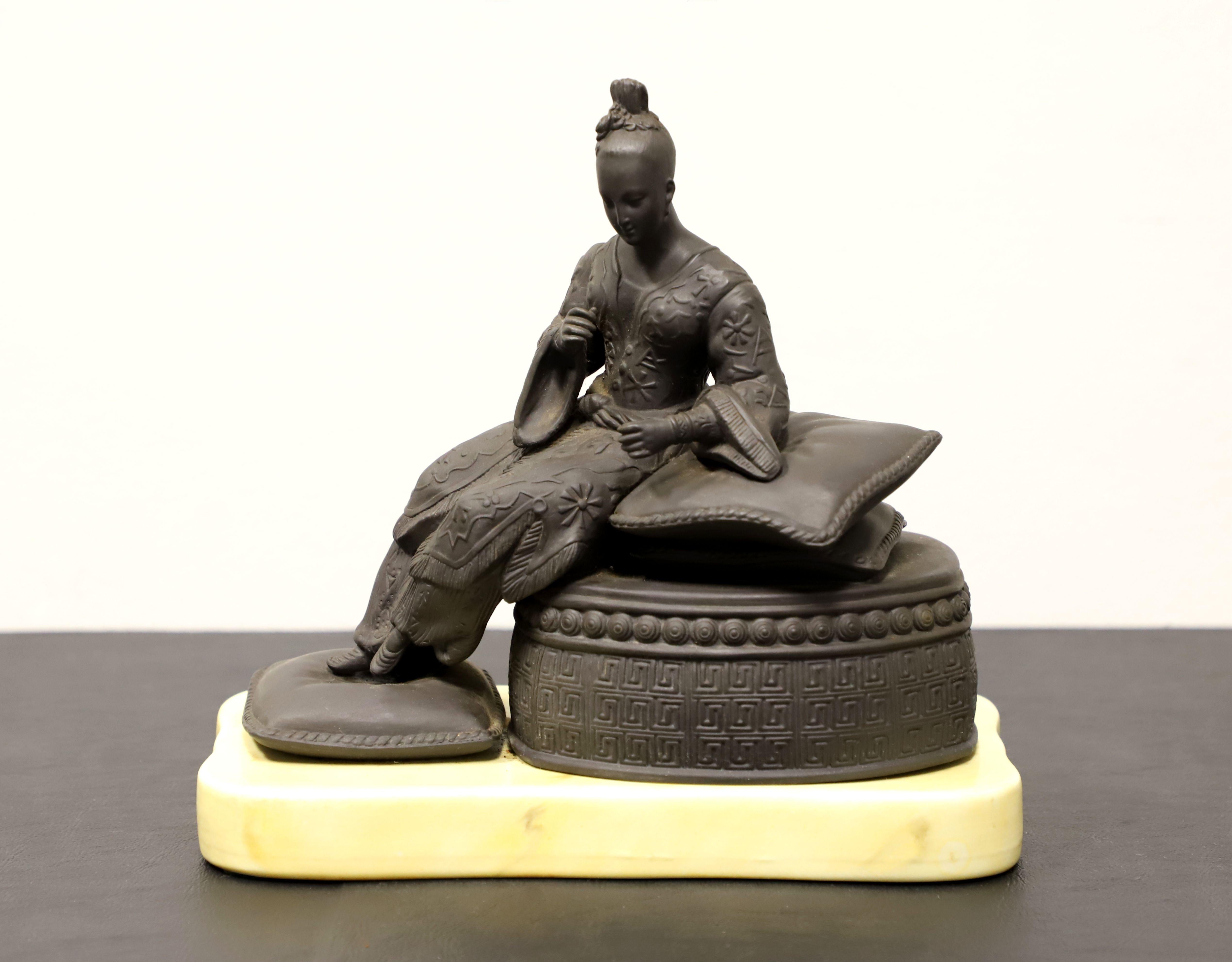 A table top sculpture by Mottahedeh. Hand carved from black basalt depicting an elegantly dressed woman reclining on pillows atop a round ottoman with her feet resting on a pillow. Sculpture is mounted to a creamy white color porcelain base. Made in