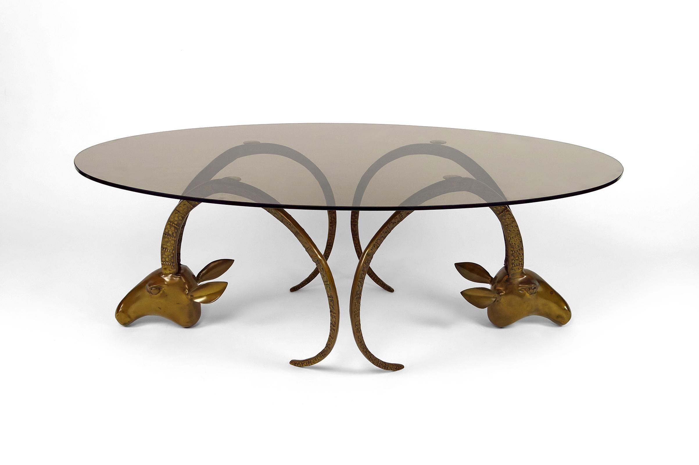 Superb coffee table composed of a pair of goat head sculptures (mouflons / ibex / antelopes) and a glass plate.

The mouflon heads are in patinated brass / bronze.
The oval tray is in smoked glass.

Hollywood Regency / Mid-Century Modern style,
