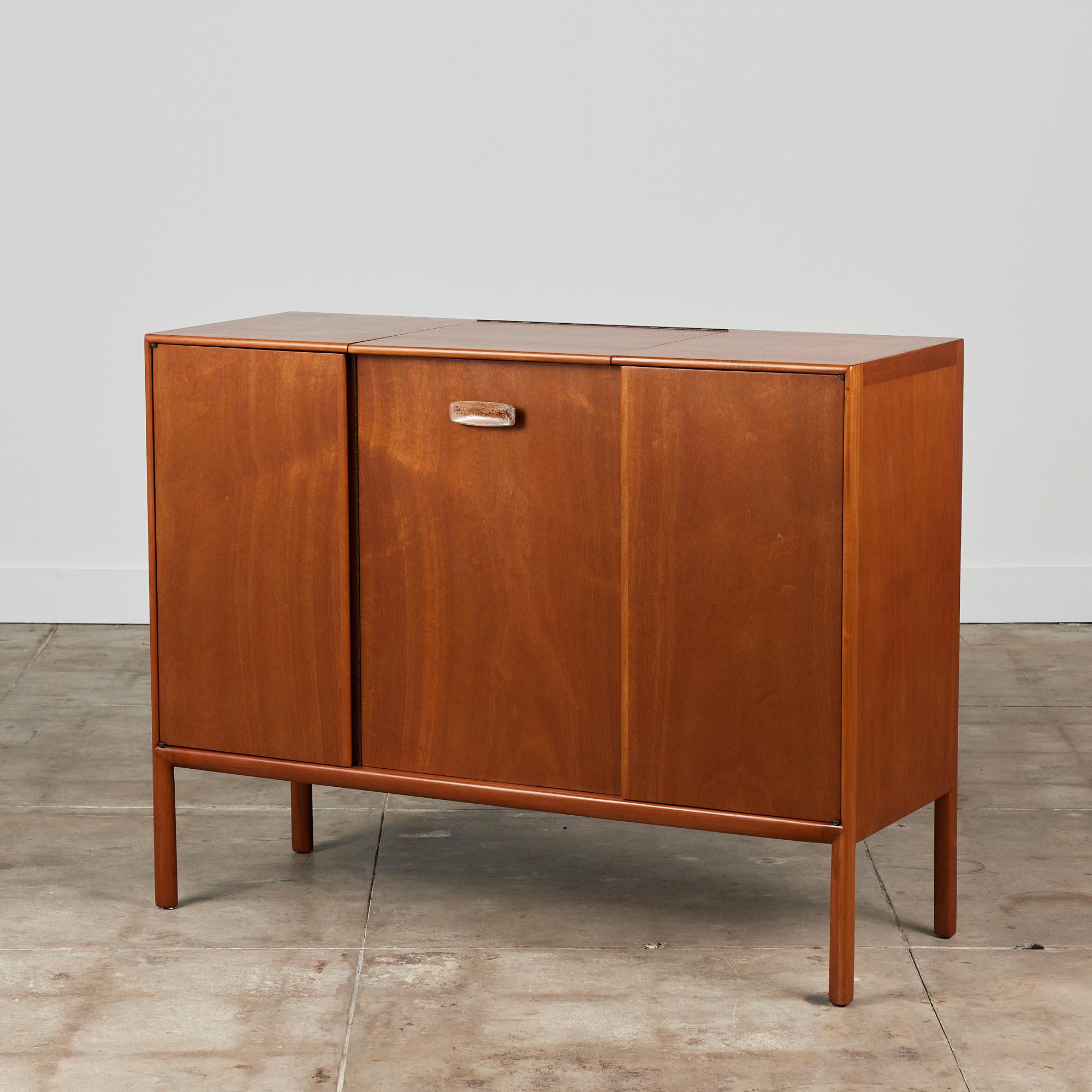 Mahogany vanity by Mount Airy Furniture, circa 1960s, USA. The dresser features three sleek door fronts which open to reveal interior storage. The center door has a brass rectangular enameled door pull. Inside the vanity is a shelf, five small