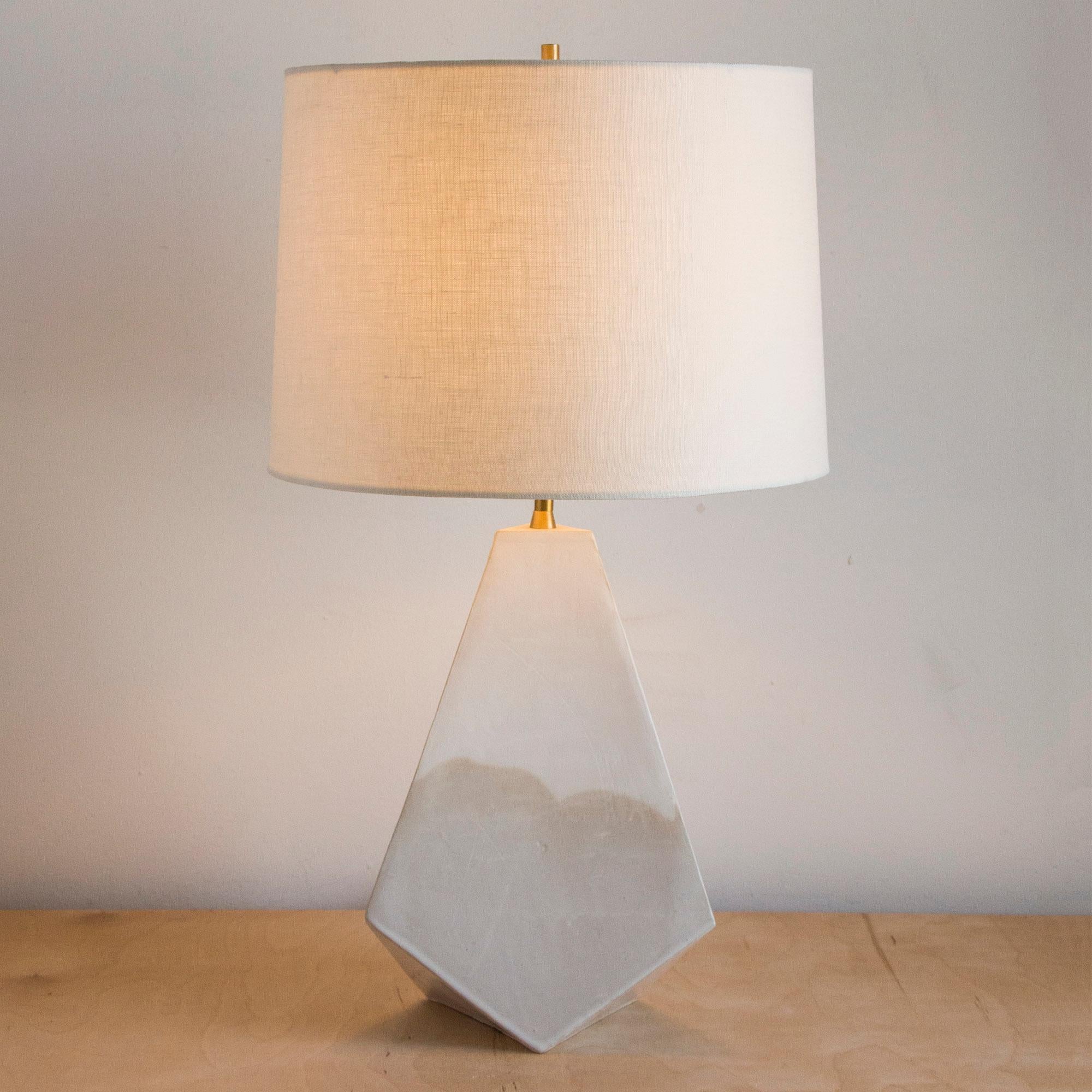 This geometric ceramic 'Mountain' table lamp is made from a sandy beige clay, formed into a dramatic pyramid shape, and featuring an organic matte finish accented by hand-poured glossy white glaze. Each piece is individually handmade and entirely