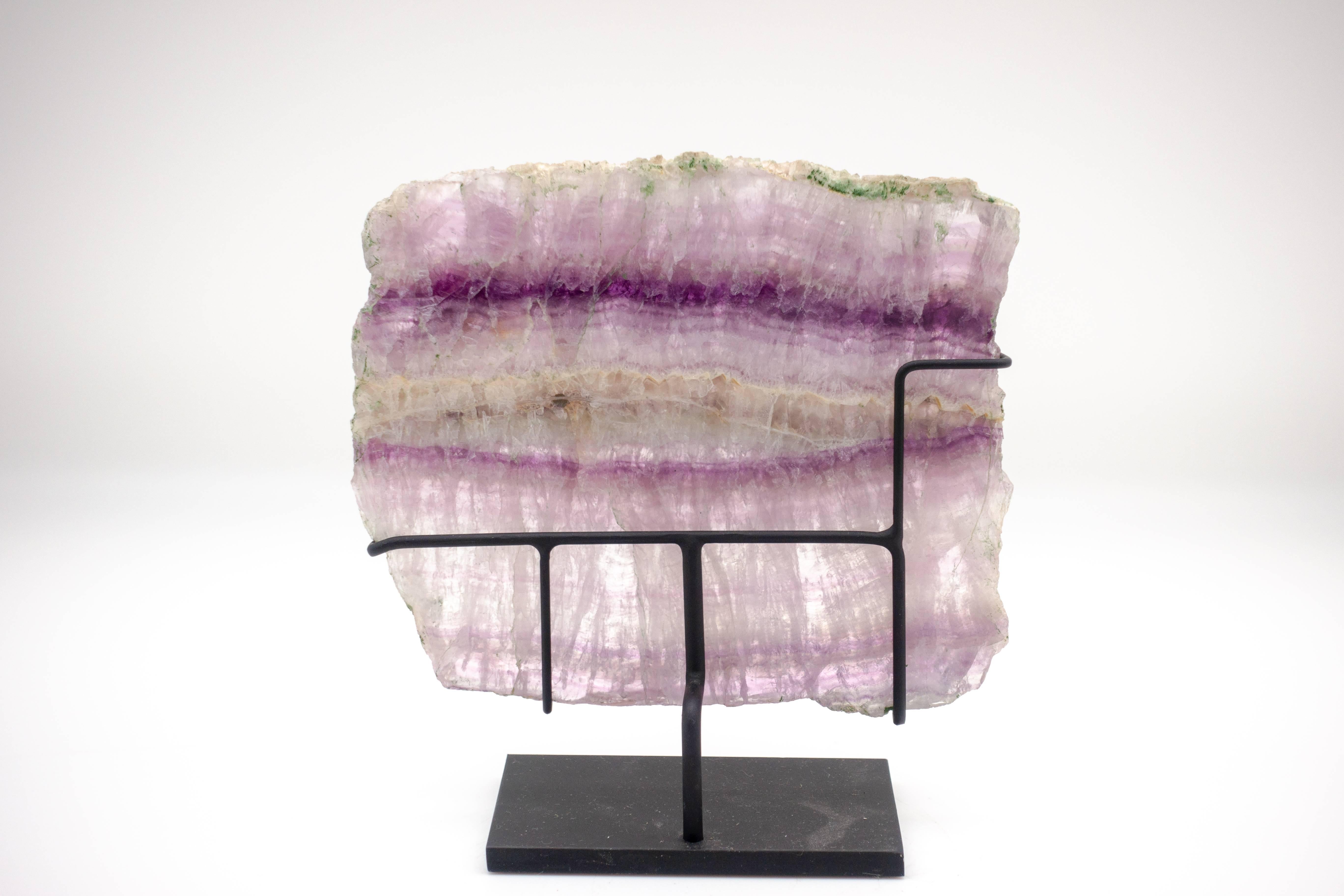 Slice of fluorite crystal mounted on a black steel base. Fluorite is a colorful mineral, used ornamentally for carvings or jewelry. Under ultraviolet light, many samples of fluorite exhibit fluorescence; the current name for this 'glow' was derived