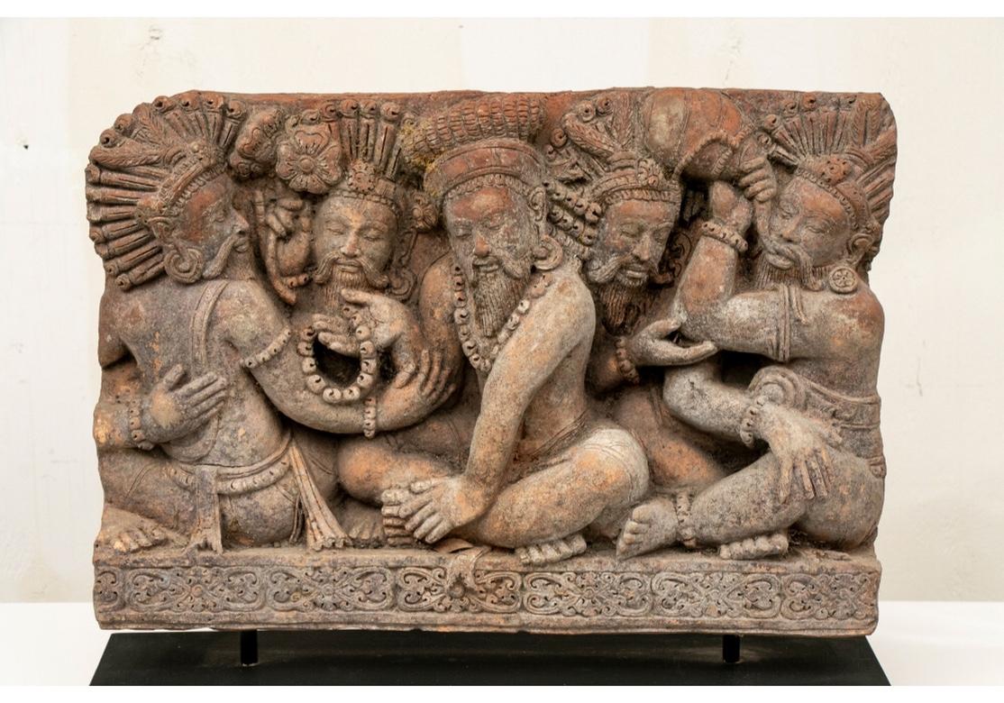 A finely modeled terracotta panel depicting five bell clad Holy Men with closed eyes and in seated postures, seemingly lost in ecstasy. The central figure sits with legs crossed in an attitude of repose or worship, his right hand holding the bell