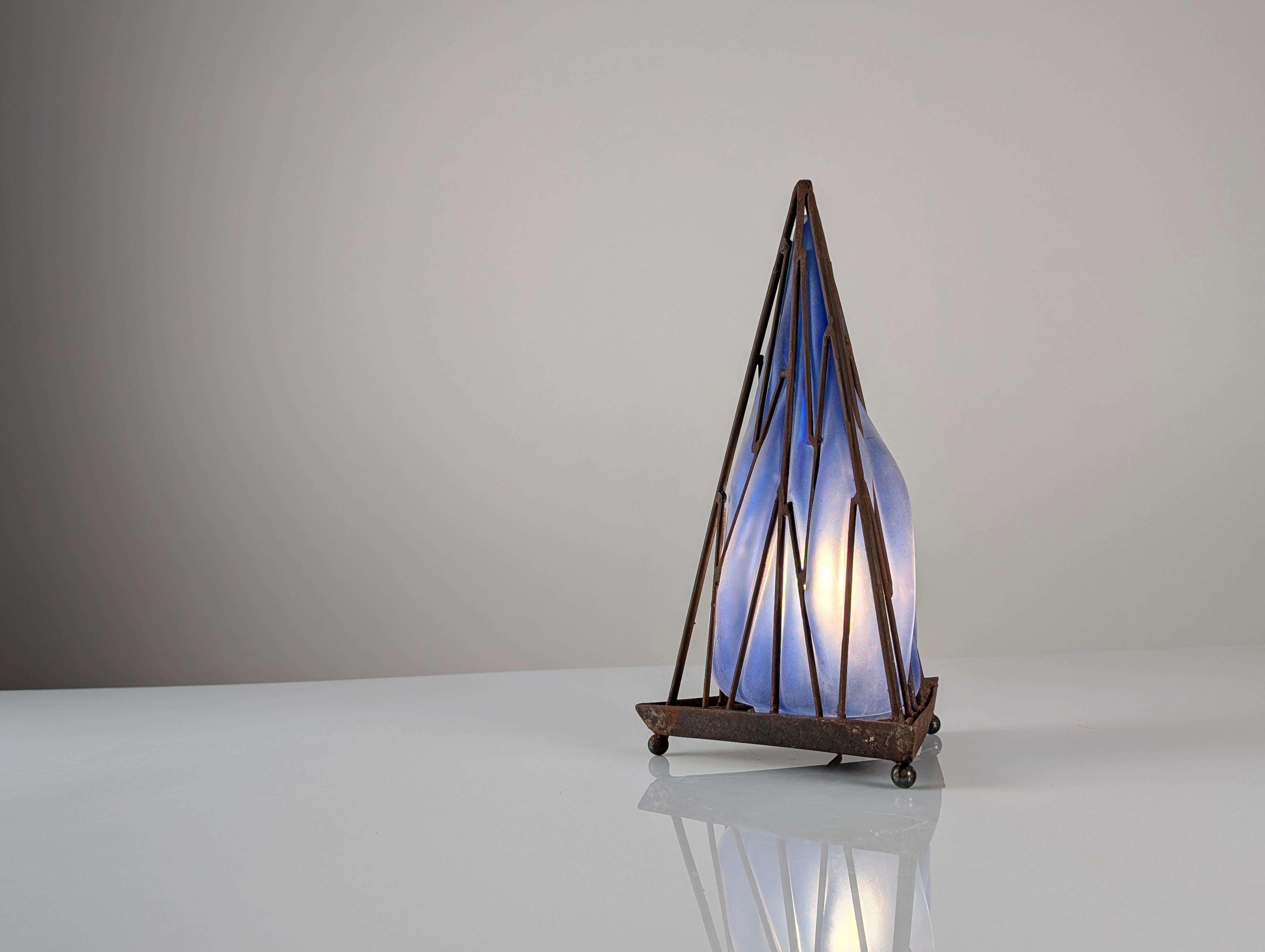 Cette étonnante lampe de table vintage présente un cadre pyramidal géométrique en fer qui renferme un éblouissant abat-jour en verre bleu soufflé à la bouche. La ferronnerie crée un beau contraste artistique avec le verre bleu lisse, qui diffuse la