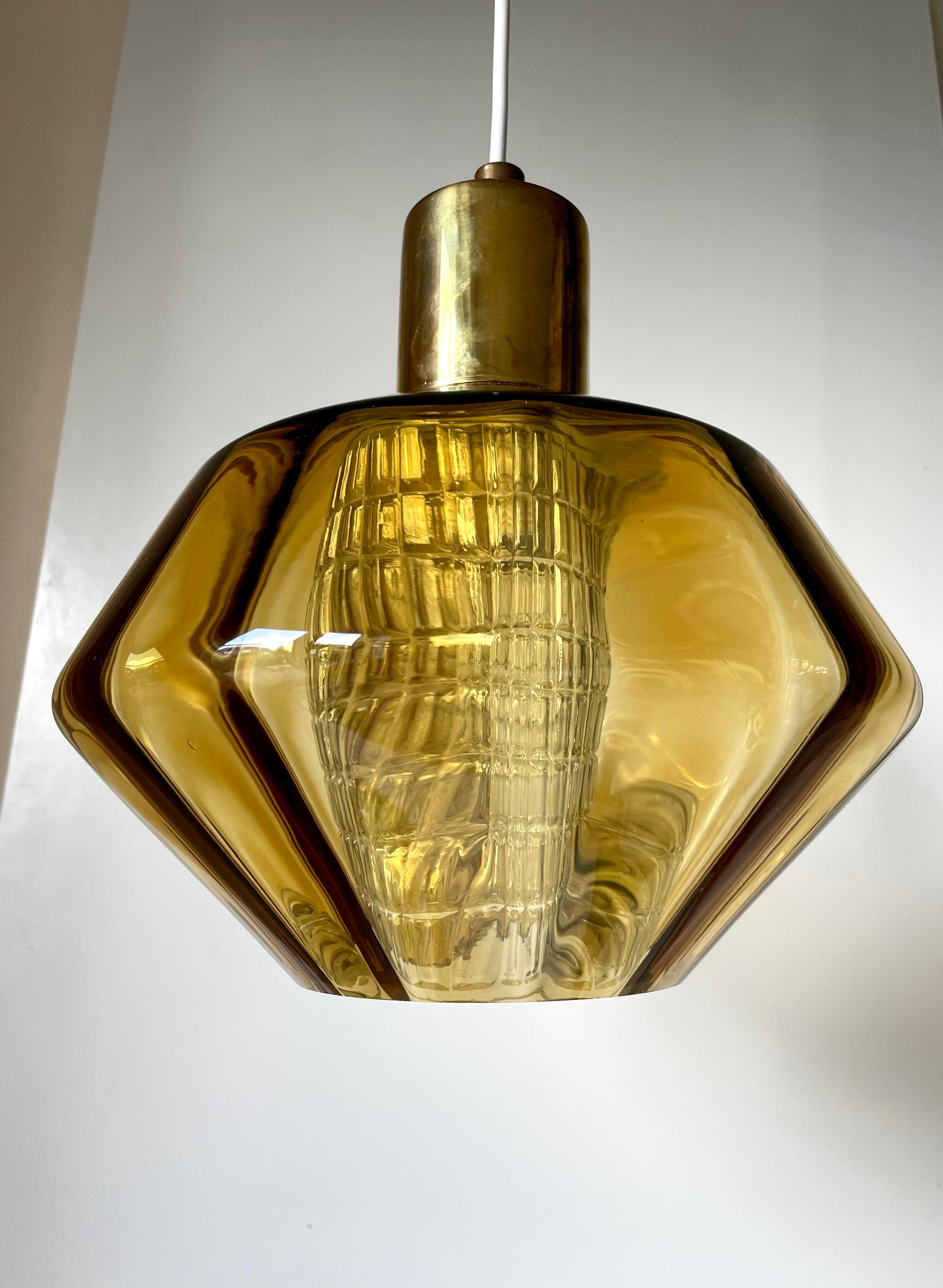 Swedish midcentury modern regency art glass pendant manufactured by Orrefors in the 1950s. Cylinder shaped clear textured glass within a mouthblown shade of thick amber colored soft angled glass. Brass top. Rewired with original fitting for E27