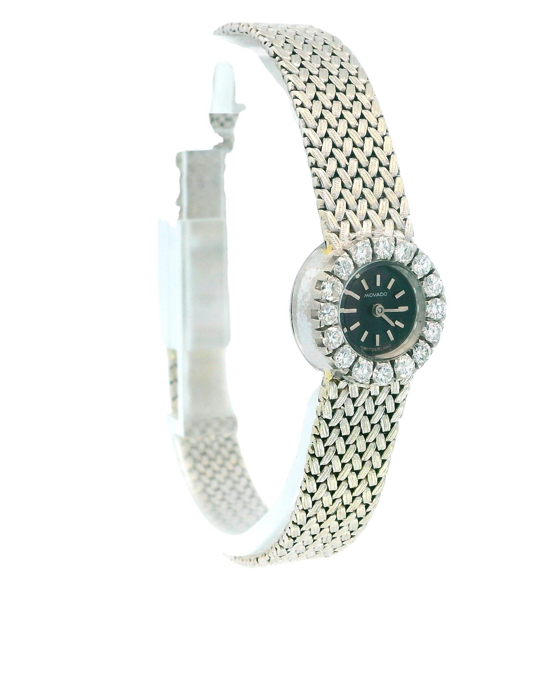 A round 18k gold watch by Movado, featuring a black dial with stick indexes. The bezel is adorned with round white diamonds, totaling 0.64 carats, with VS1 clarity and H color grade. The case is crafted from 18k white gold, complemented by a snap