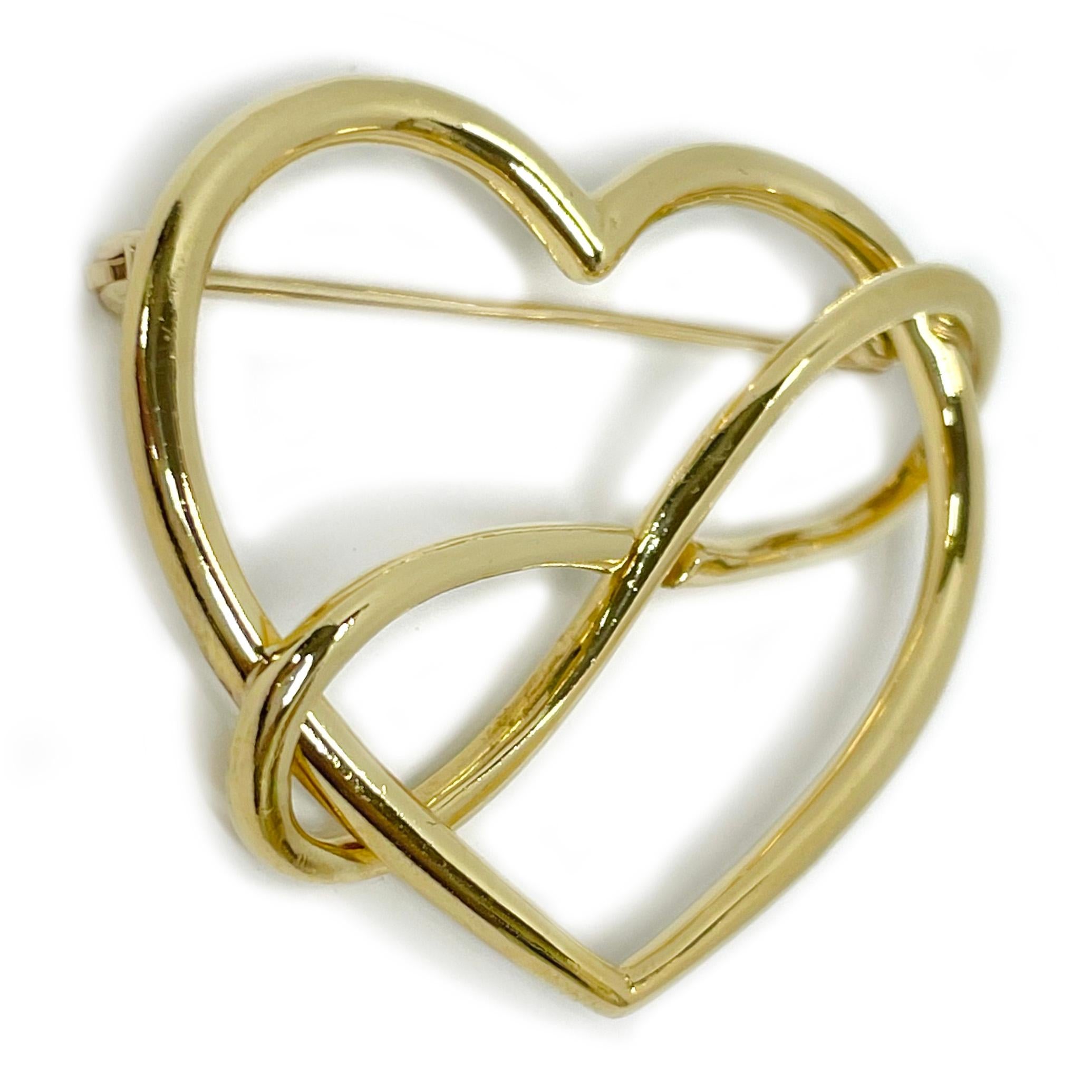 18 Karat Movado Yellow Gold Heart Infinity Brooch. The heart is made of a tubular shaped gold with an infinity loop interlocked diagonally across the heart. The brooch features two interlocking loops that create a heart. Stamped on the back of the