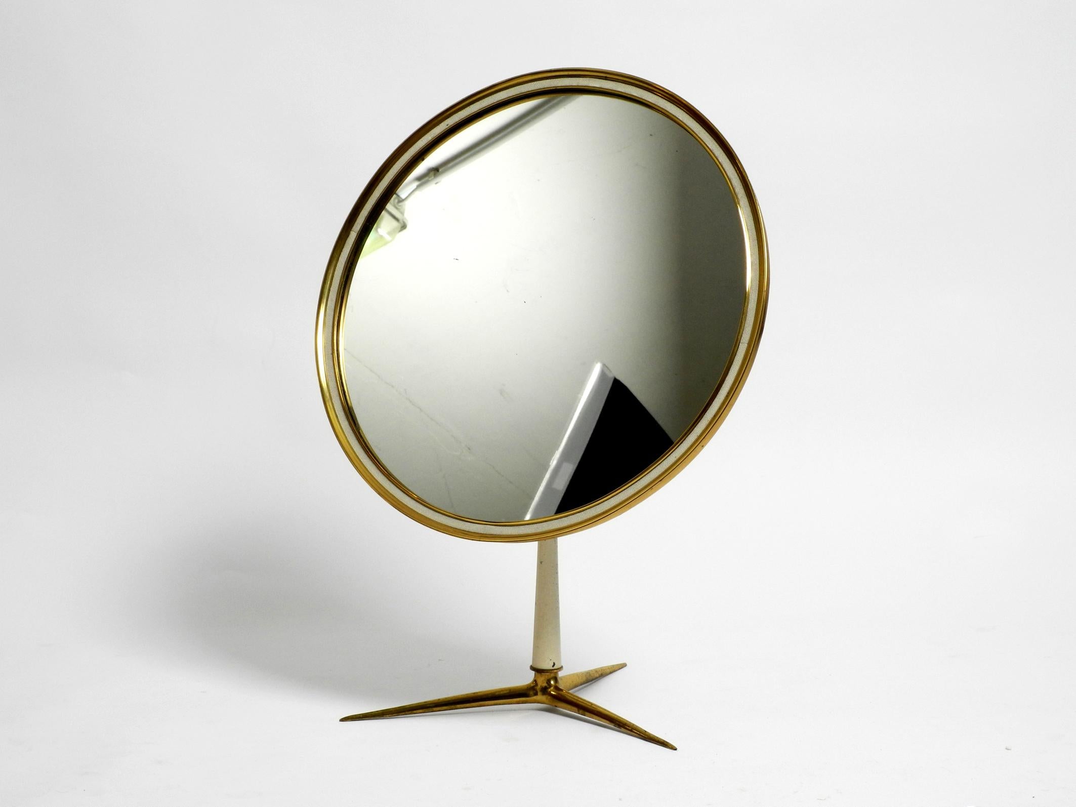 Beautiful, very rare, large, moveable, midcentury, three-legged base table mirror.
Manufacturer is Vereinigten Werkstätten. Made in Germany.
In the typical 1950s design with a round brass frame.
Heavy brass mirror frame and base. Cast aluminum