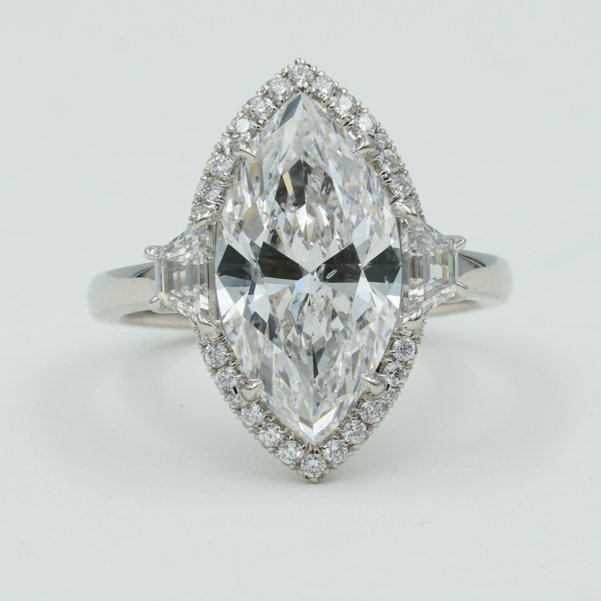 Dieser STUNNING Drei-Stein-Verlobungsring verfügt über einen schillernden 5,02ct Marquise geschnittenen Mittelstein mit zwei spitz zulaufenden Baguette-Diamanten an den Seiten des Mittelsteins, die insgesamt 0,52 Karat. Der Mittelstein hat eine