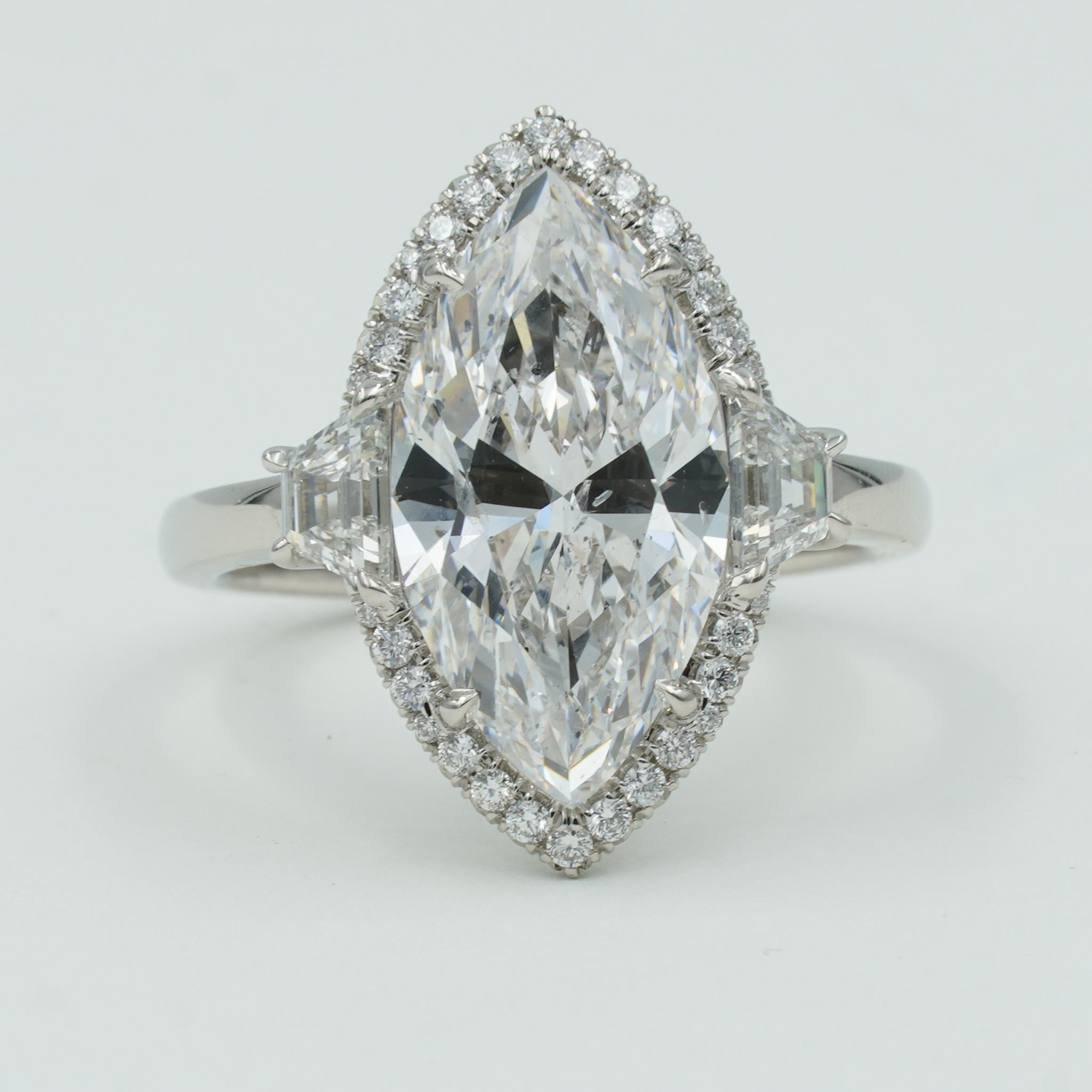 This STUNNING three-stone engagement ring features a dazzling 5.02ct marquise cut center stone with two tapered baguette diamonds on the sides of the center stone that total 0.52 carats. The center stone is E in color, SI2 in clarity, and is