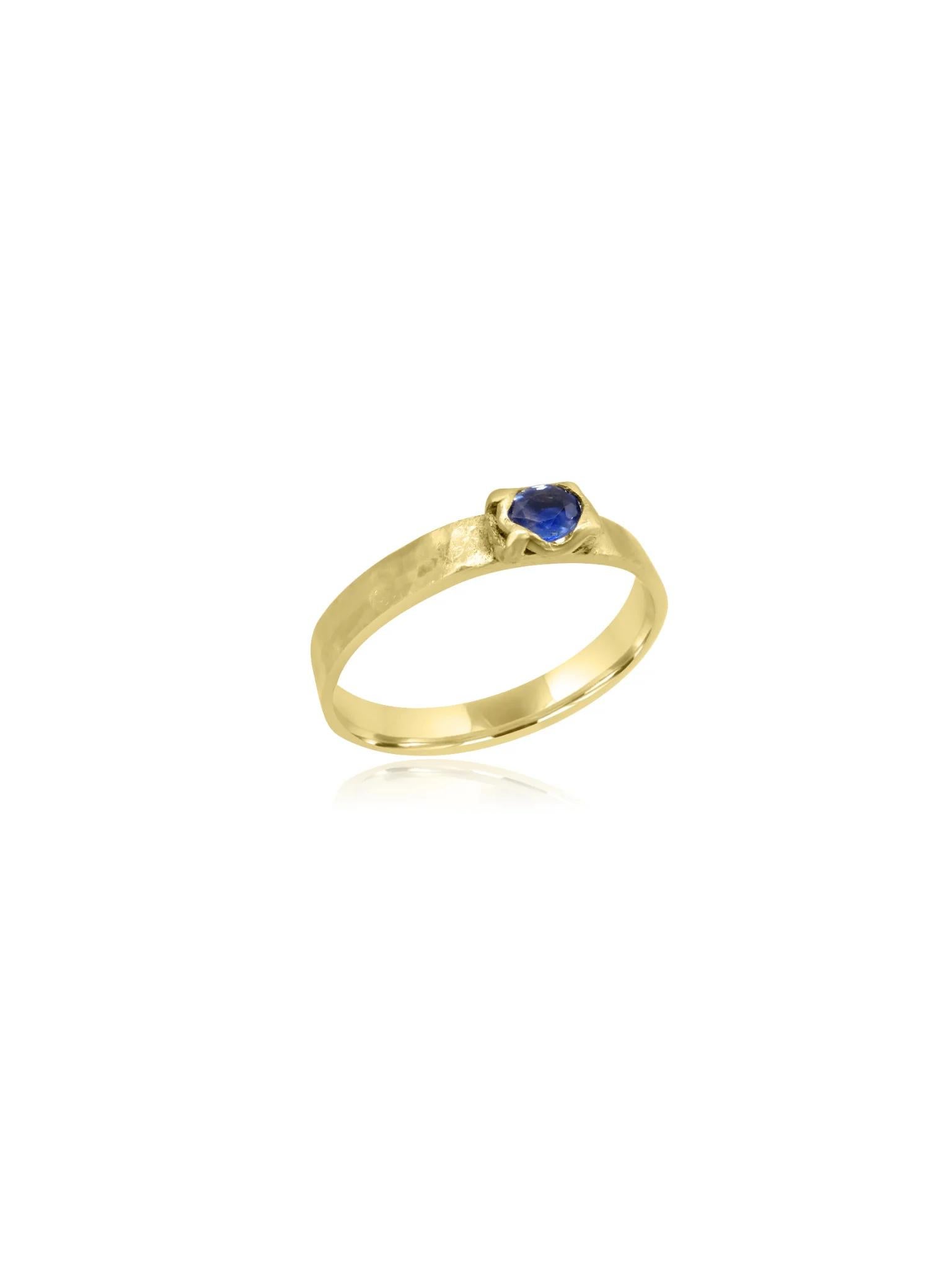 Stunning ring crafted from 18 karat textured gold in Cornwall. The thick band features a unique texture, adding depth and character to the design. At the centre, a beautifully set round-cut blue sapphire stone catches the eye, providing a striking