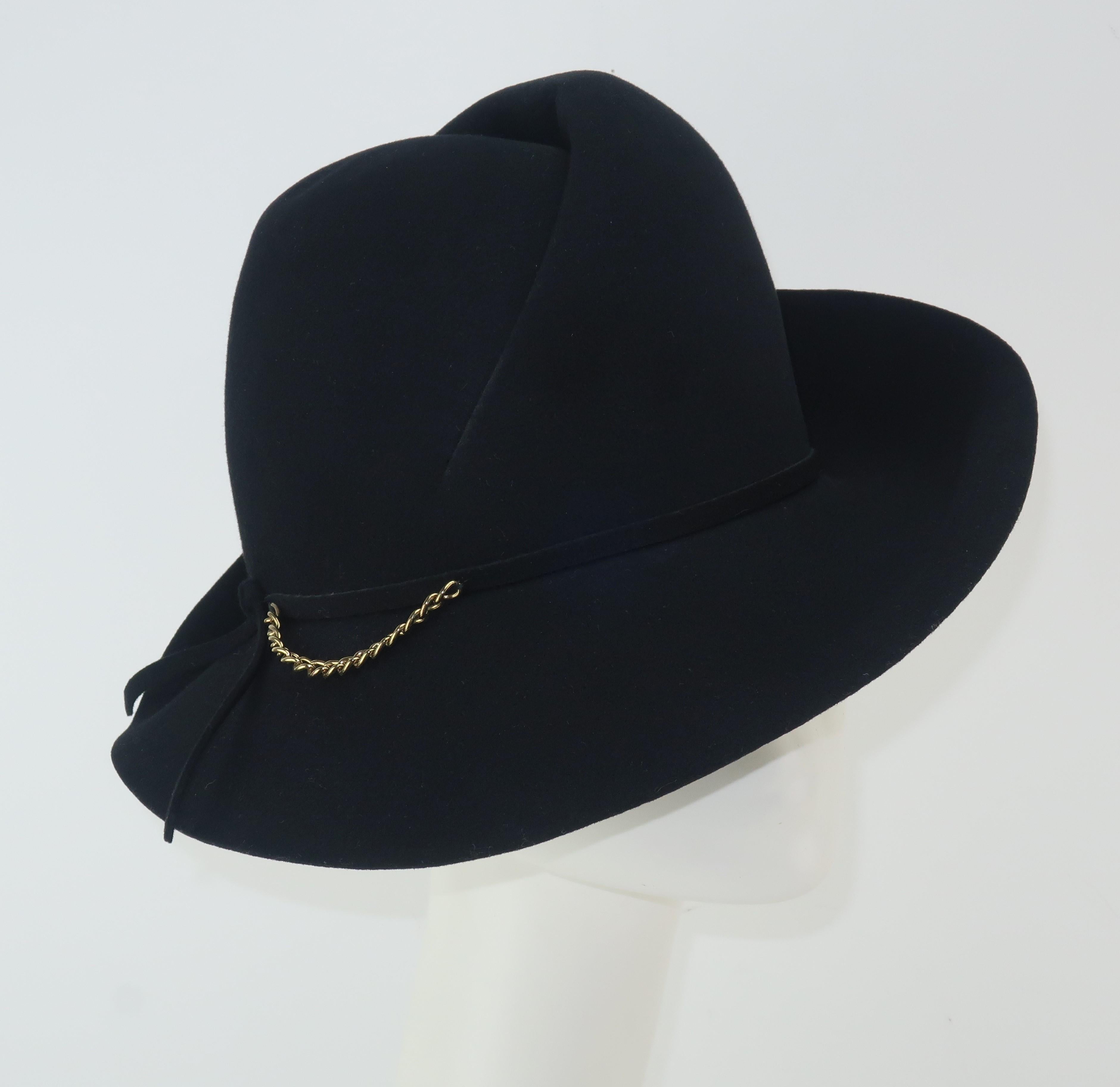 A stylized 1960's black felt fedora by John Harberger for his millinery line, Mr. John Classics.  The sculptural construction of the hat along with a gold tone chain embellishment provides an updated femininity to a classic menswear look.  The hat