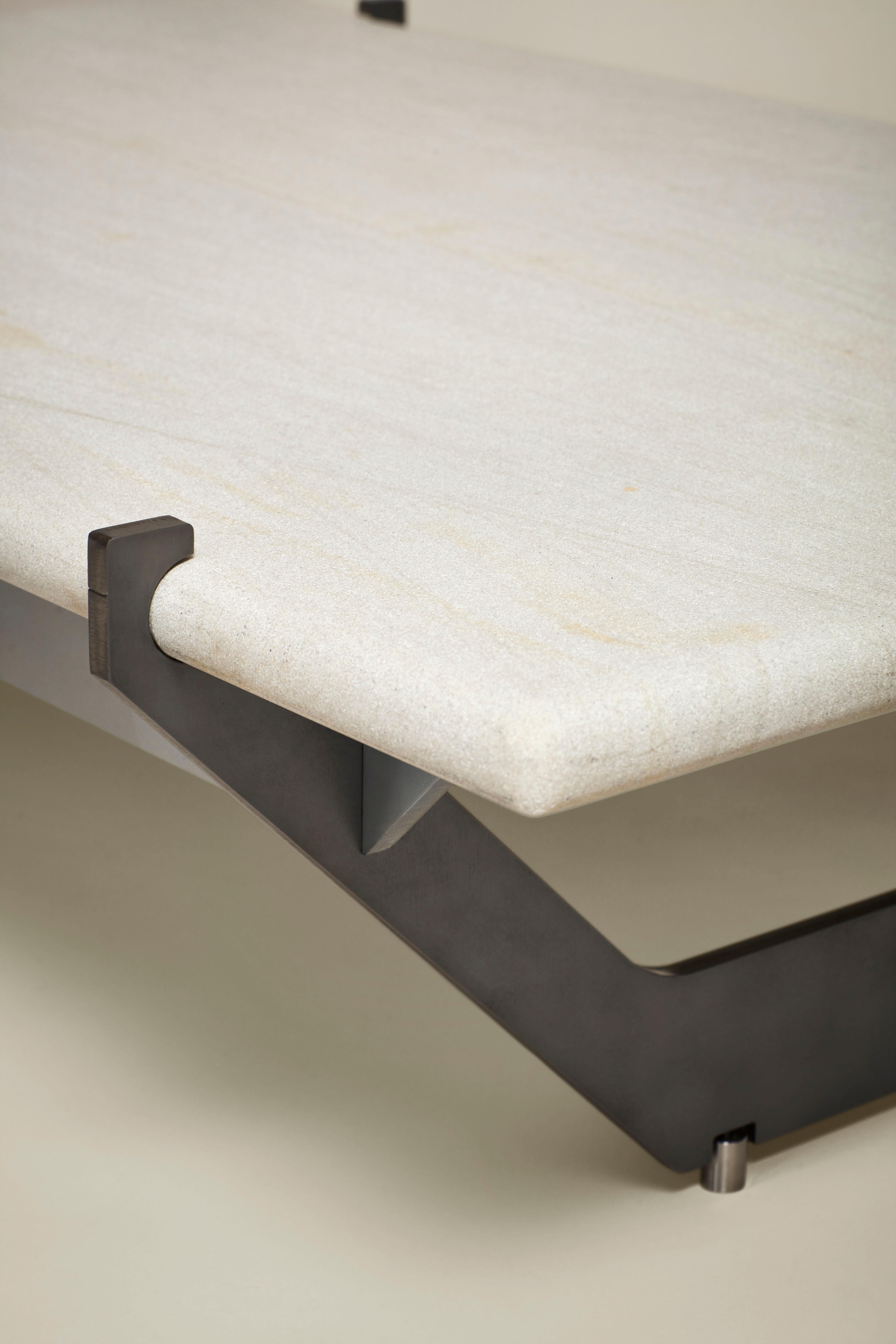 Il tavolino MŪ311 trae ispirazione dalle qualità planari della struttura della base del letto MŪ11 e ne reinterpreta il design con una combinazione di acciaio e pietra. Il modo in cui il piano del tavolo in pietra è fissato alla base è esagerato