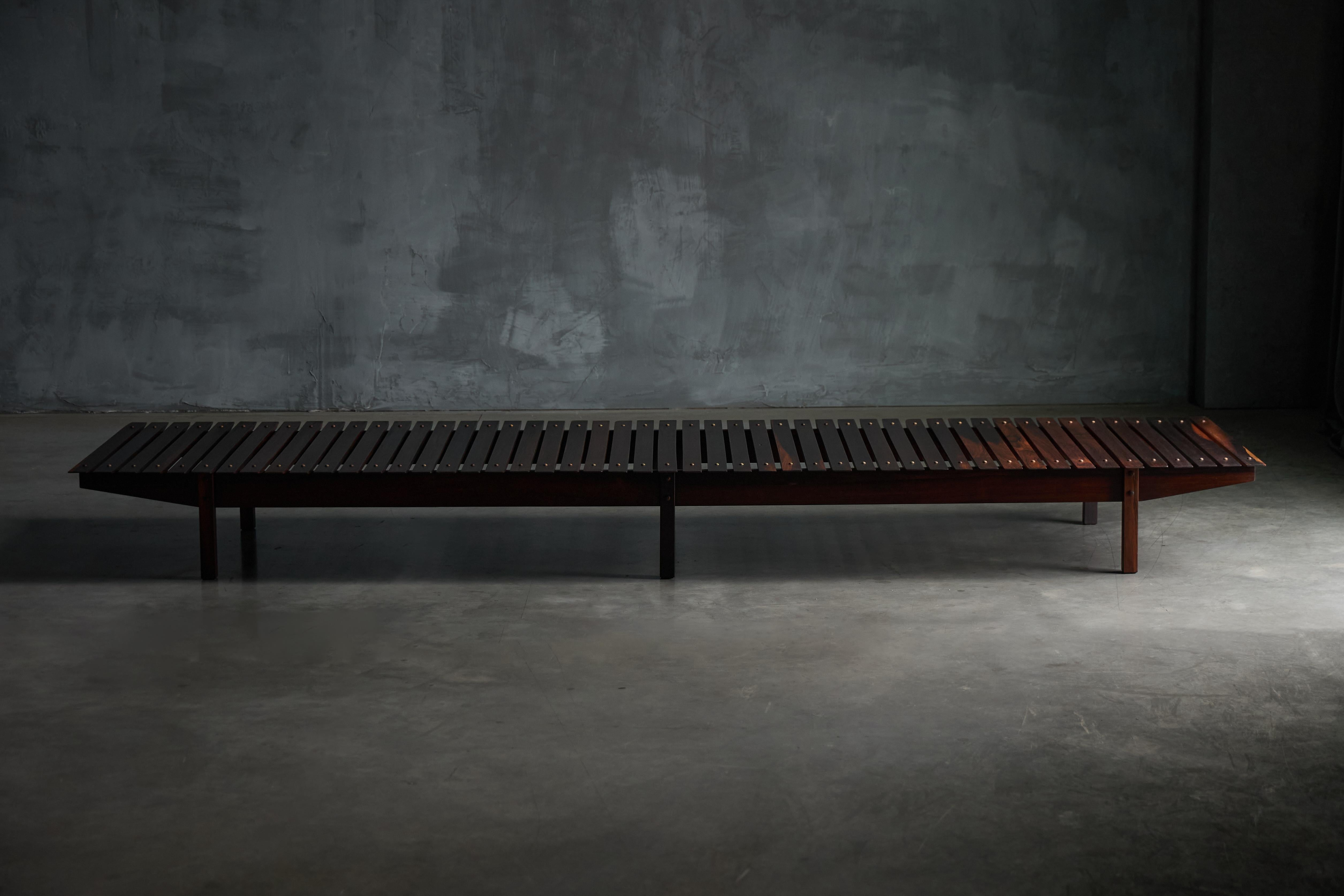 Originally designed circa 1958 and produced around 1965 by OCA Industrias Reunidas, the Mucki Bench by Sergio Rodrigues is a rare and versatile piece crafted in massive Brazilian wood and veneer. With its low, slatted design and timeless