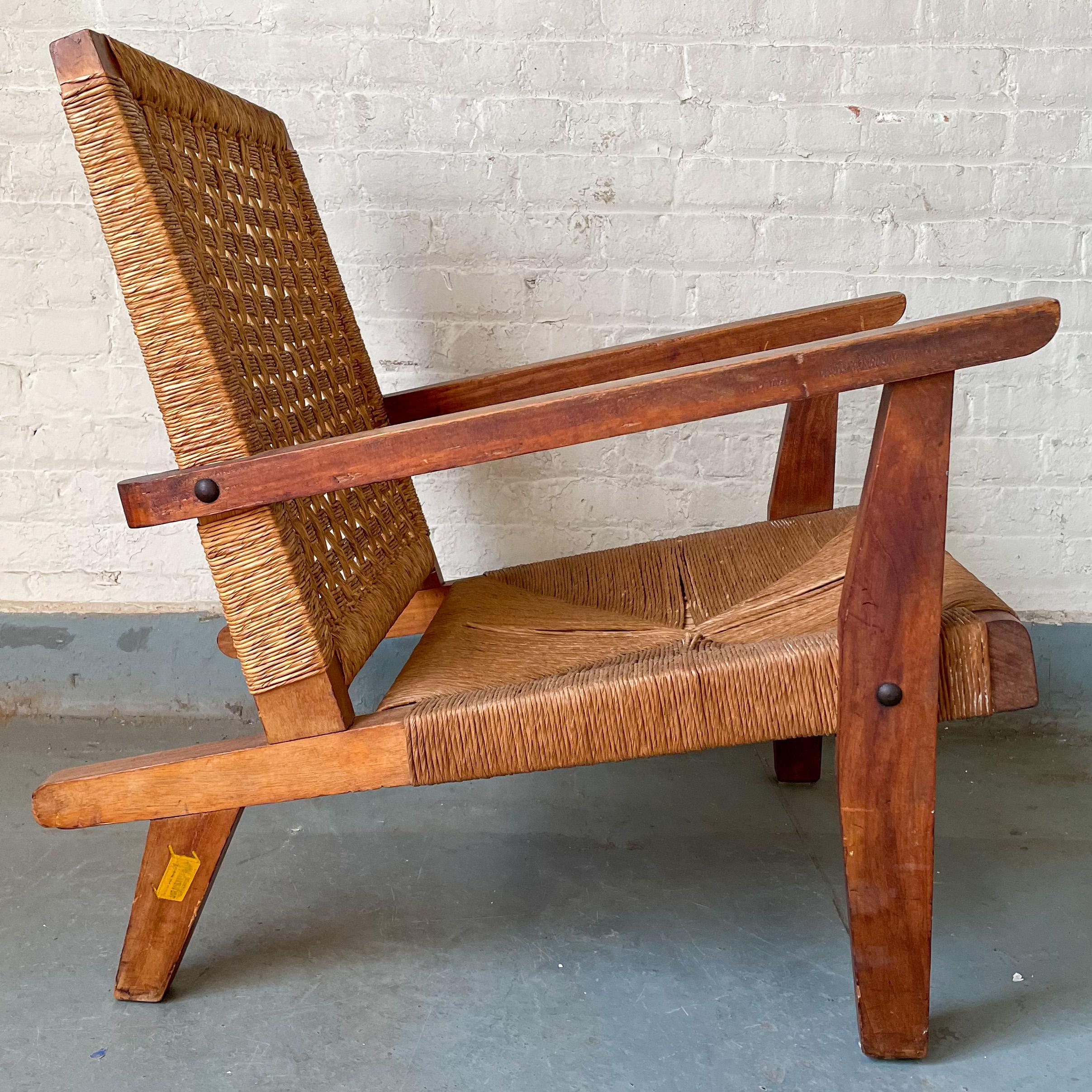 Knock-down lounge chair with arms in solid carved pine with a woven plasticized palm seat and back, in the manner of Clara Porset, produced by Muebles Austin of Mexico City, 1950’s. The chair is designed to disassemble via a loose mortise-and-tenon