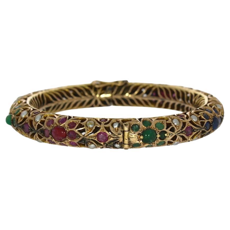 This antique Mughal bracelet bangle is a luxurious piece crafted from 14kt yellow gold, designed to showcase a vibrant collection of gemstones. The intricate openwork design is adorned with an impressive combination of colors and textures,