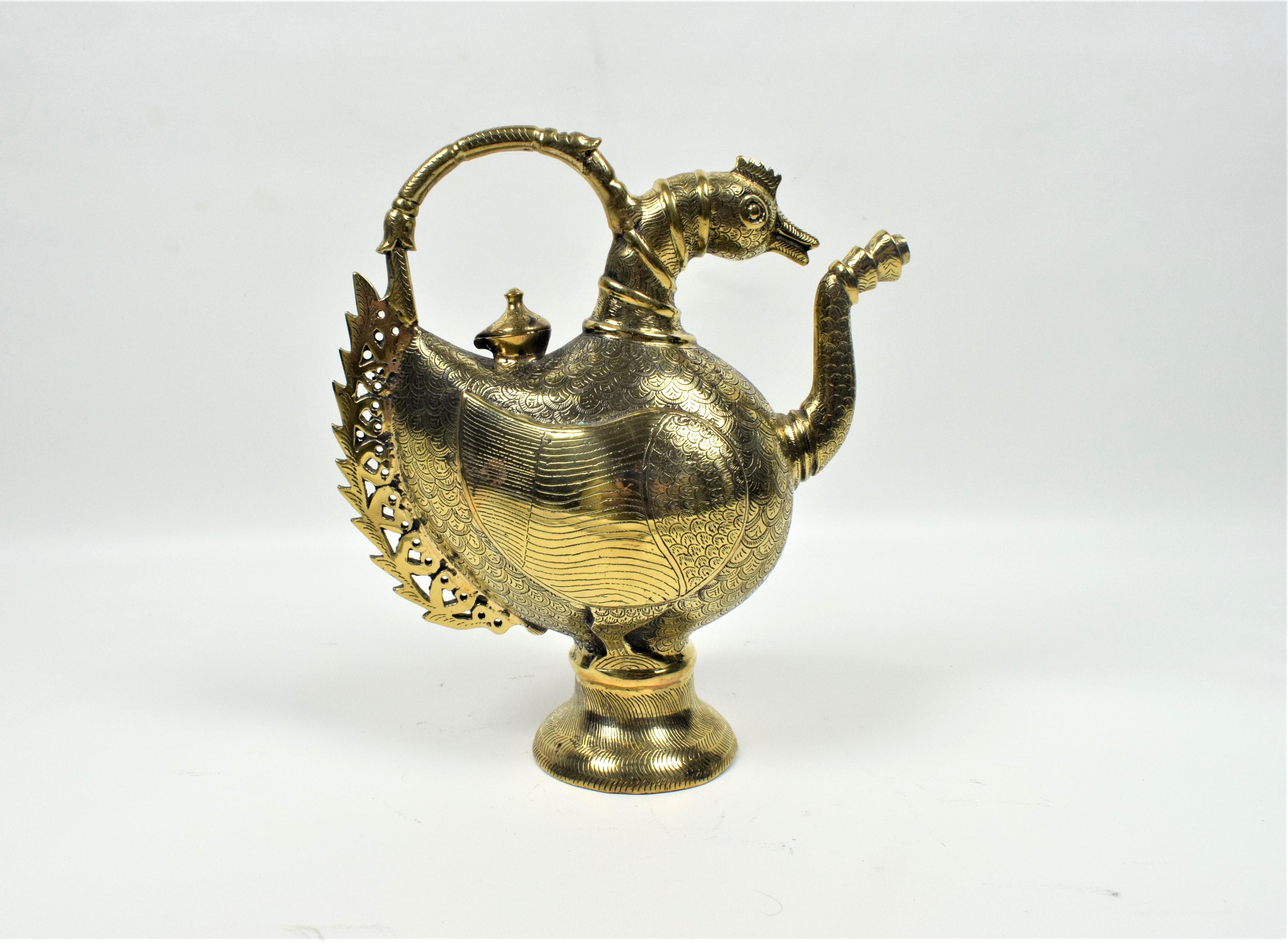 Die Kanne, ein zeremonieller Krug, hat die Form eines majestätischen Pfaus, ein bedeutendes Motiv in der Mogulkunst, das Schönheit, Anmut und Königlichkeit symbolisiert. Der Korpus der Kanne ist aus hochwertigem Messing gefertigt, einem Metall, das