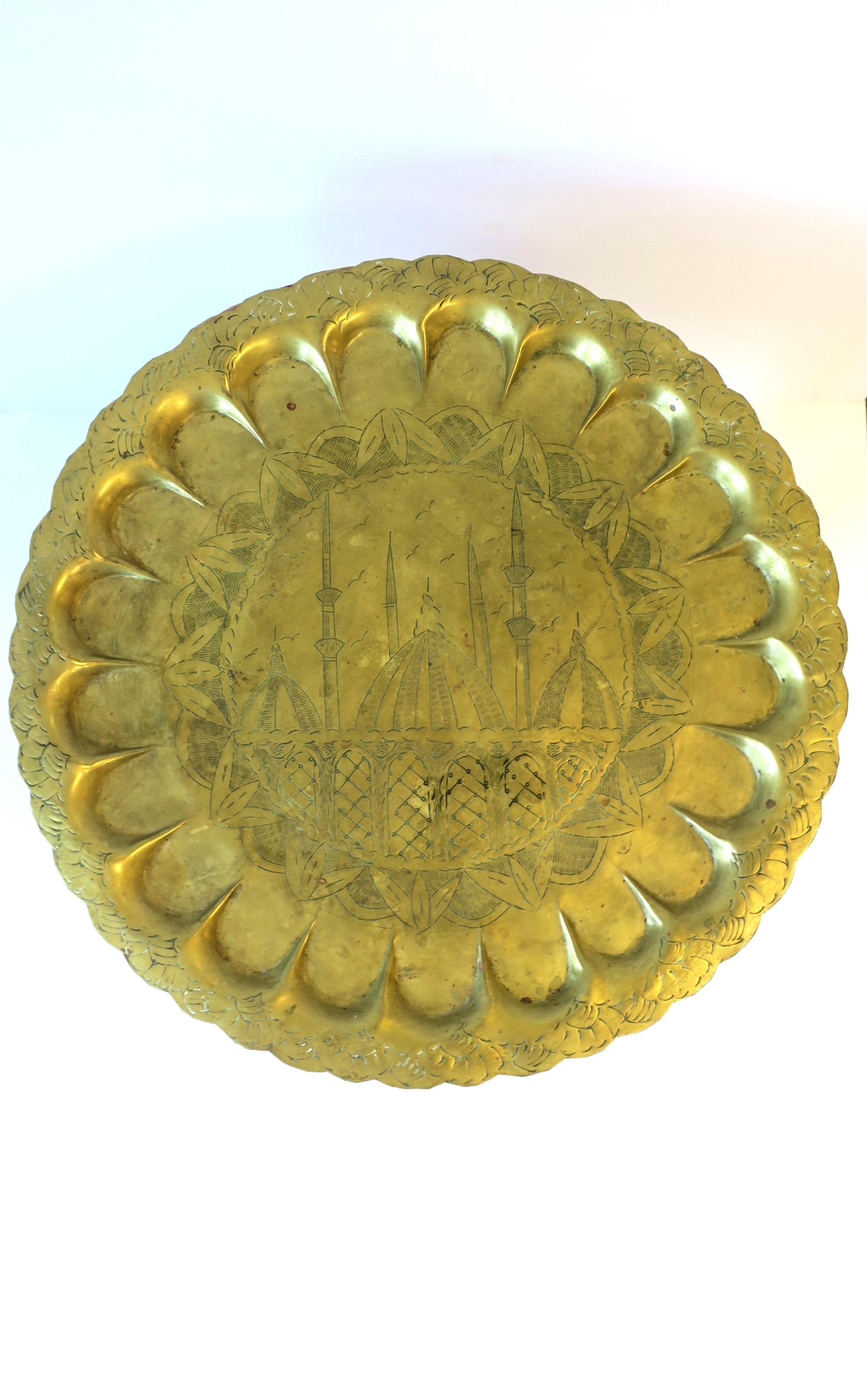 A round brass serving tray or decorative wall art piece, circa early to mid-20th century. Brass tray is round with a Mughal or Moorish design. Great as a serving tray (as demonstrated) or as decorative wall art. Dimensions: 16.63