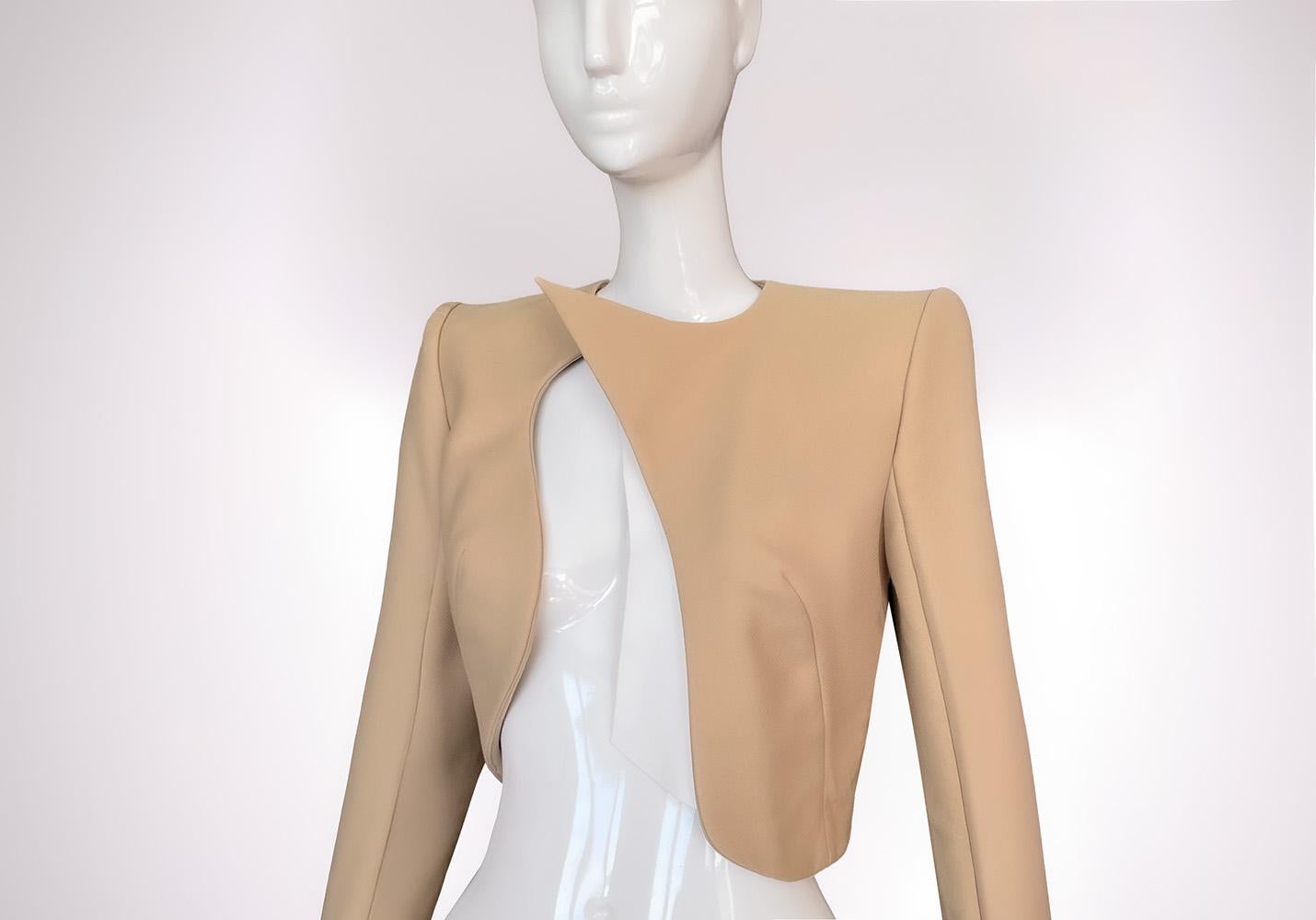 Questo  La giacca bolero di Mugler emerge come un lampo di luce del deserto: nitida, minimale ed eroticamente precisa. Fabrice Silhouette, realizzata in un morbido tessuto color beige/sabbia, aderisce al corpo con la disciplina dell'alta moda e